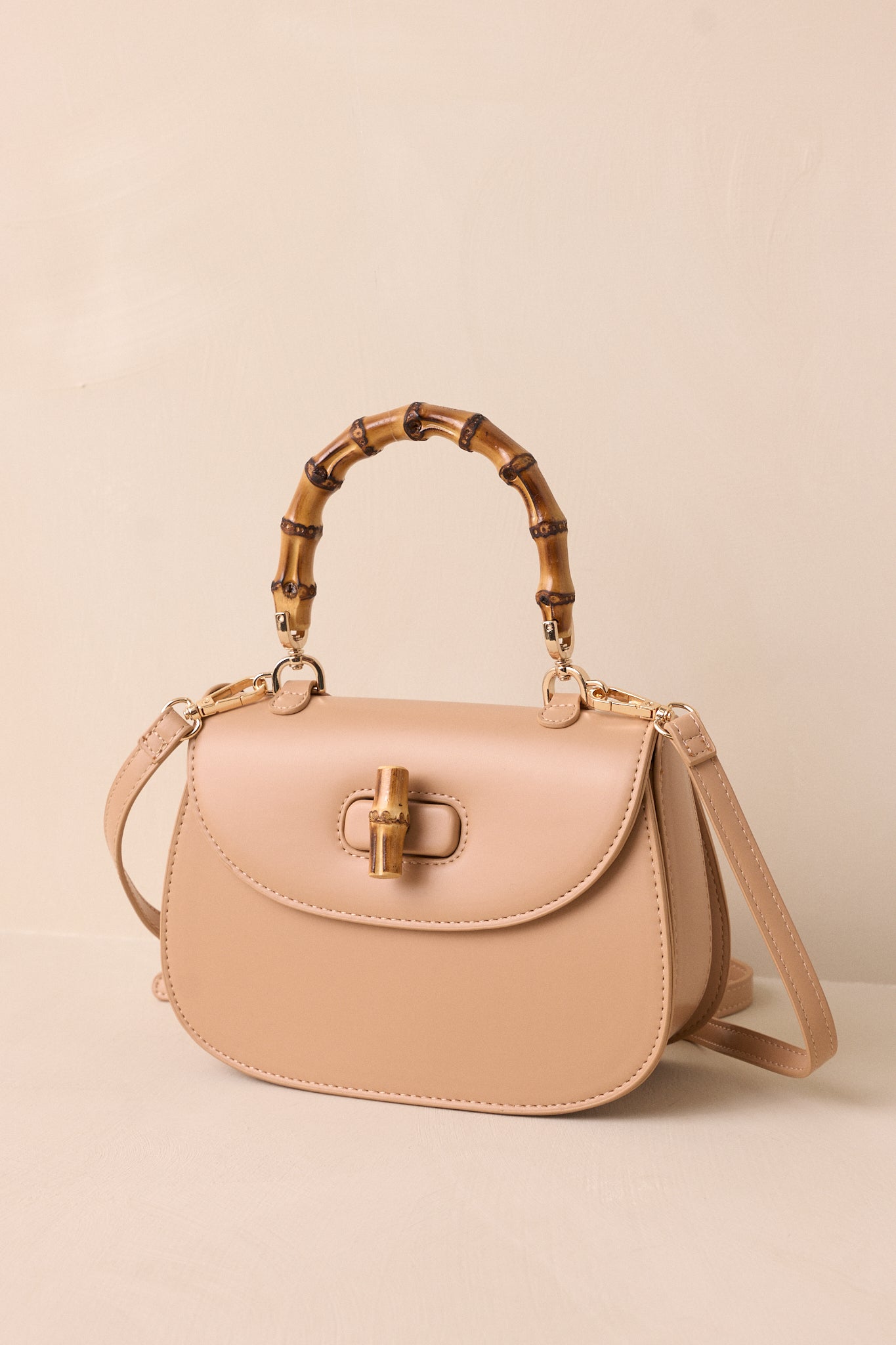 A cropped view of the beige handbag highlighting the bamboo top handle and removable strap.