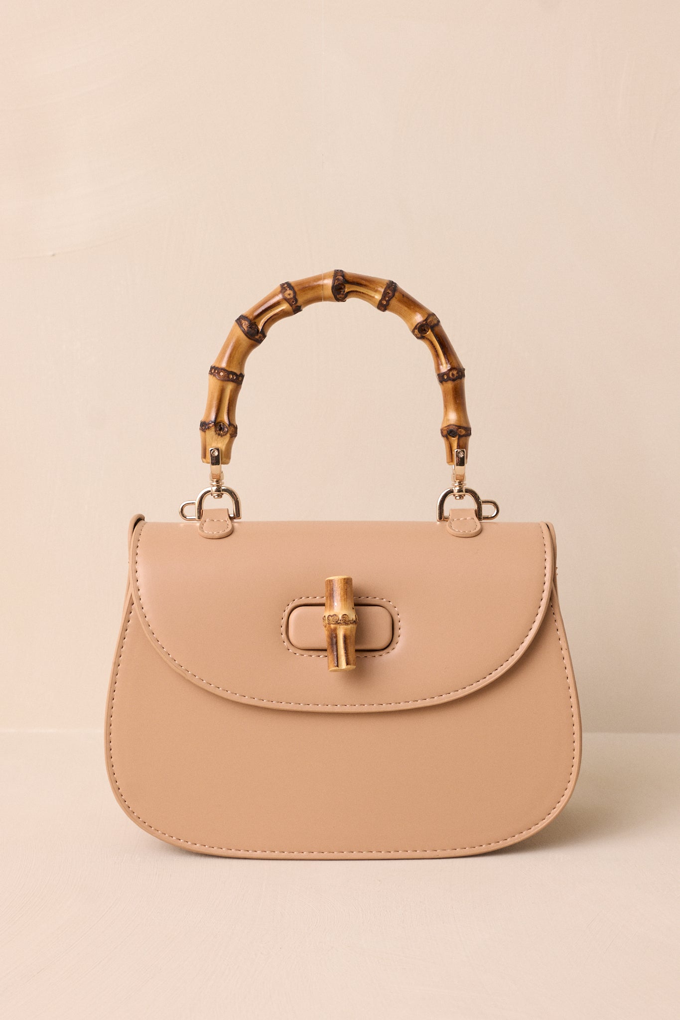 A close-up of the beige handbag's single flap design and bamboo twist lock closure in focus.