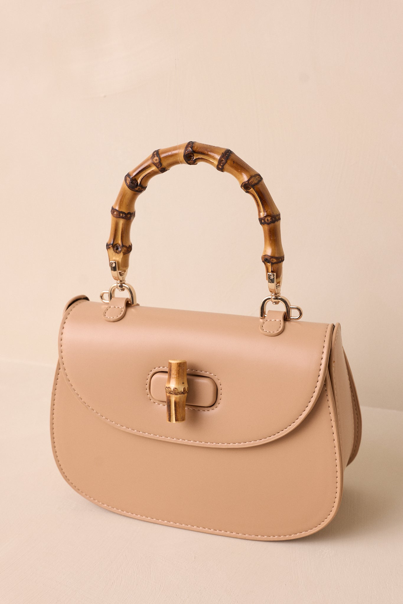 A cropped angled view of the beige handbag highlighting the bamboo top handle and removable strap.