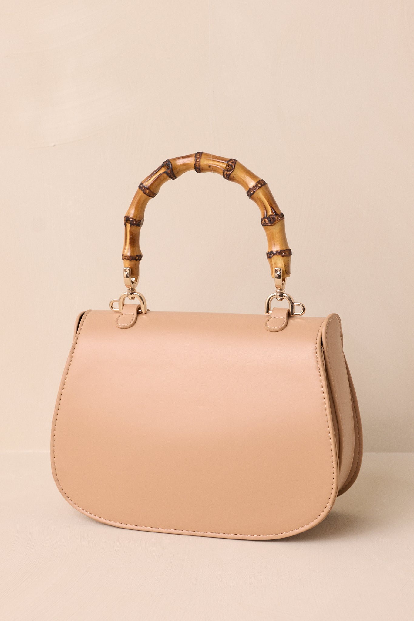 A rear view of the beige handbag emphasizing its smooth back panel and removable strap attachment.