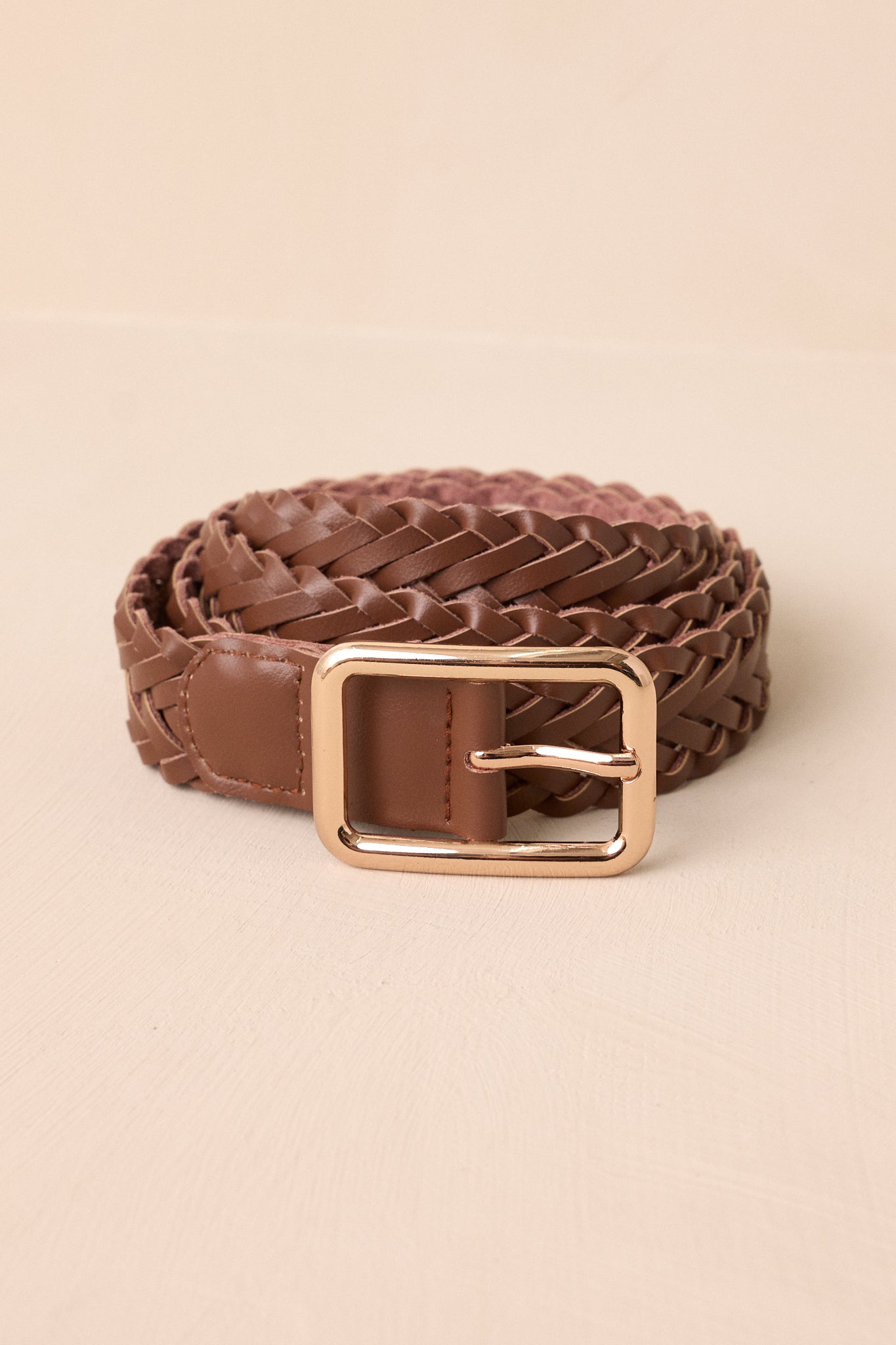 Close-up of this braided dark brown belt that features a gold hardware rectangular buckle and a brown braided material.