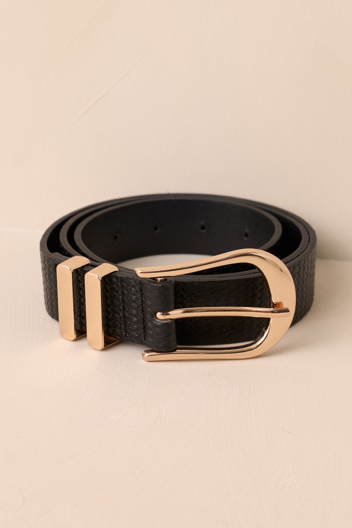 Front view of an black woven belt featuring a gold hardware buckle, a black inside, a woven texture, and two gold belt loops.