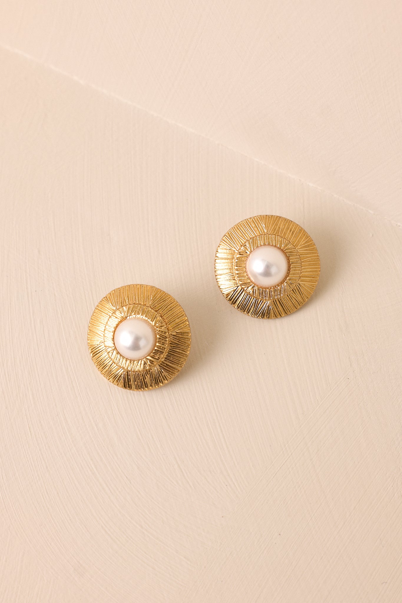 Front view of the gold earrings, highlighting the intricate texture of the sun ray pattern and the luminous faux pearl centerpiece.