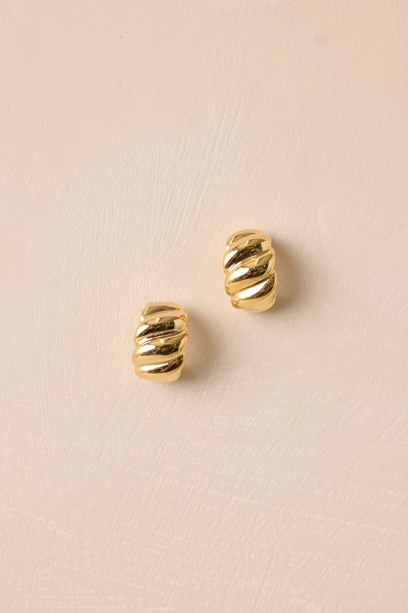 Angled shot of the gold earrings, emphasizing the gentle curve of the twist design in a polished gold tone.