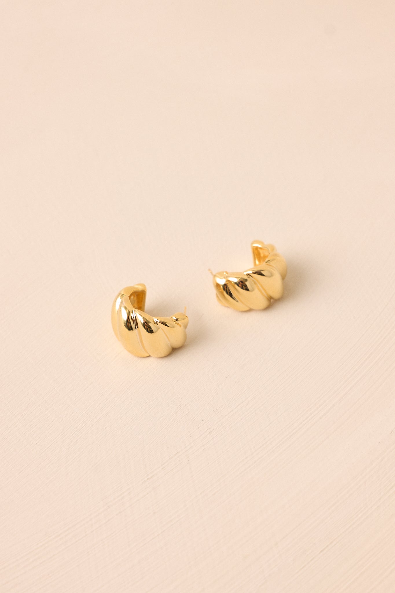 Side view of the gold earrings, showing the twist design along the half hoop structure with a smooth finish.