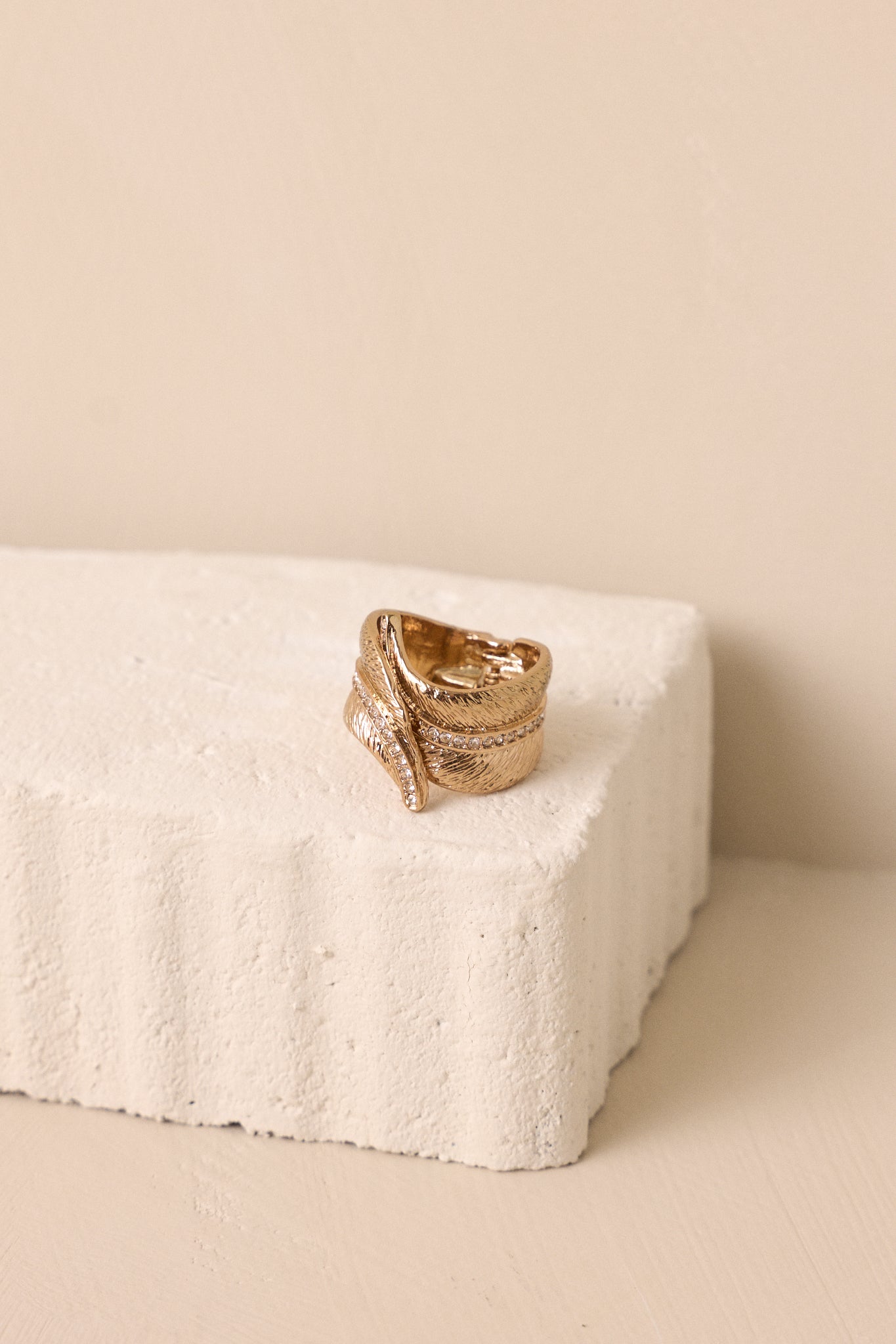 Gold ring in the shape of a feather that wraps around the finger, with a split band and rhinestones through the middle of the feather. 