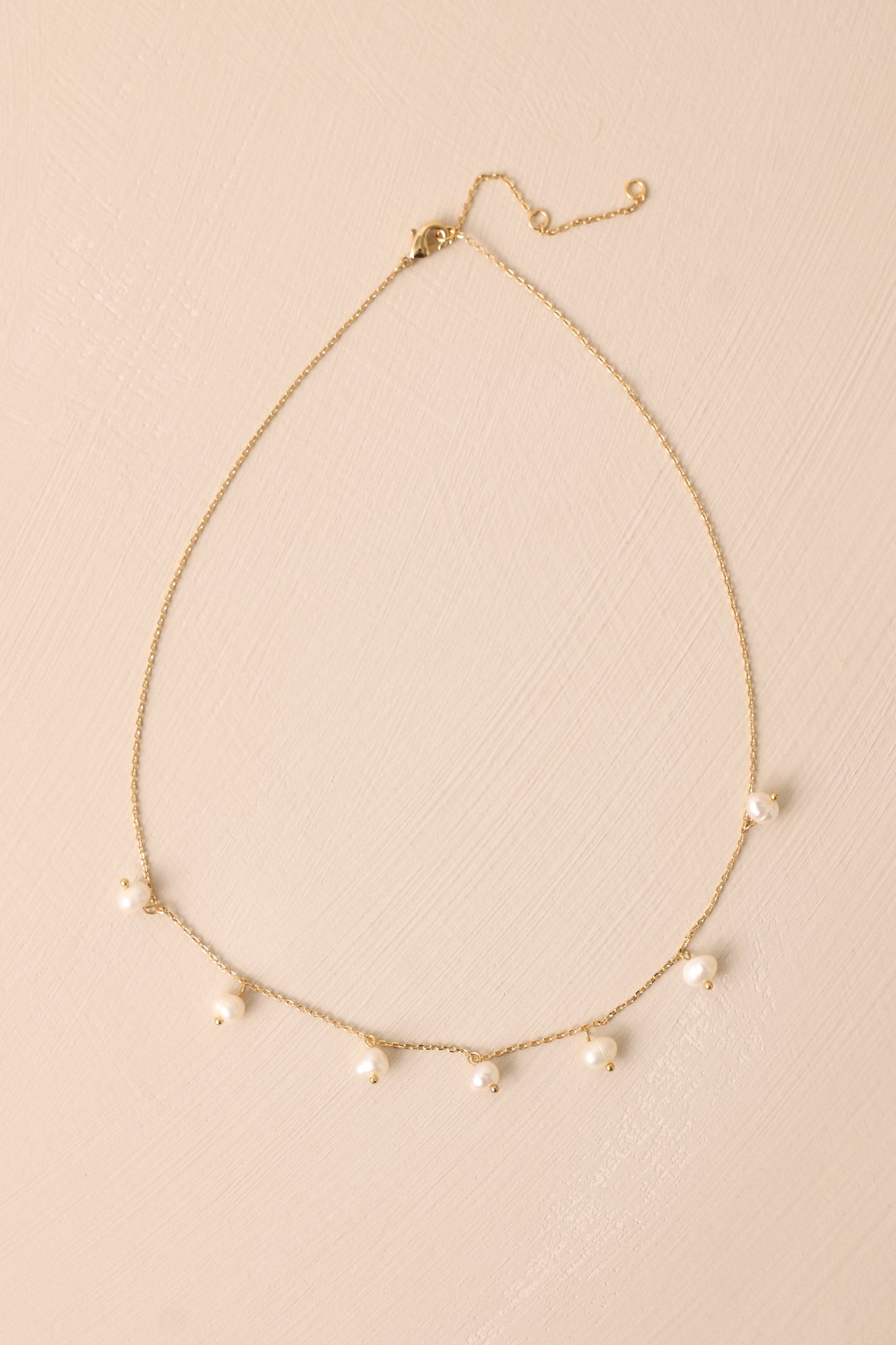 Close-up of a gold necklace with a thin gold chain, featuring seven small dangling ivory faux pearls.