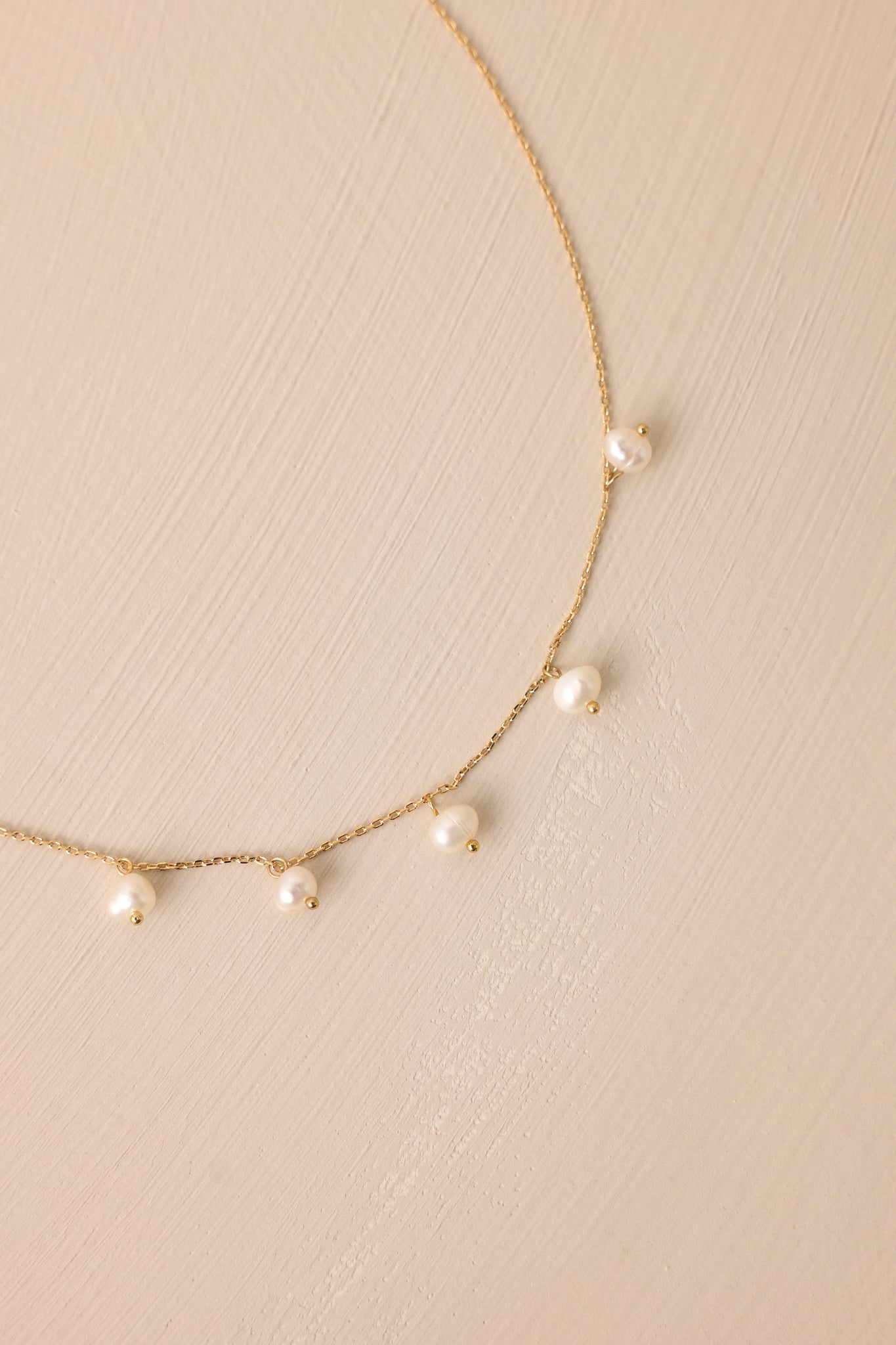 Extreme close-up of the gold necklace, highlighting the delicate thin chain and the seven small ivory faux pearls with a lobster claw clasp.