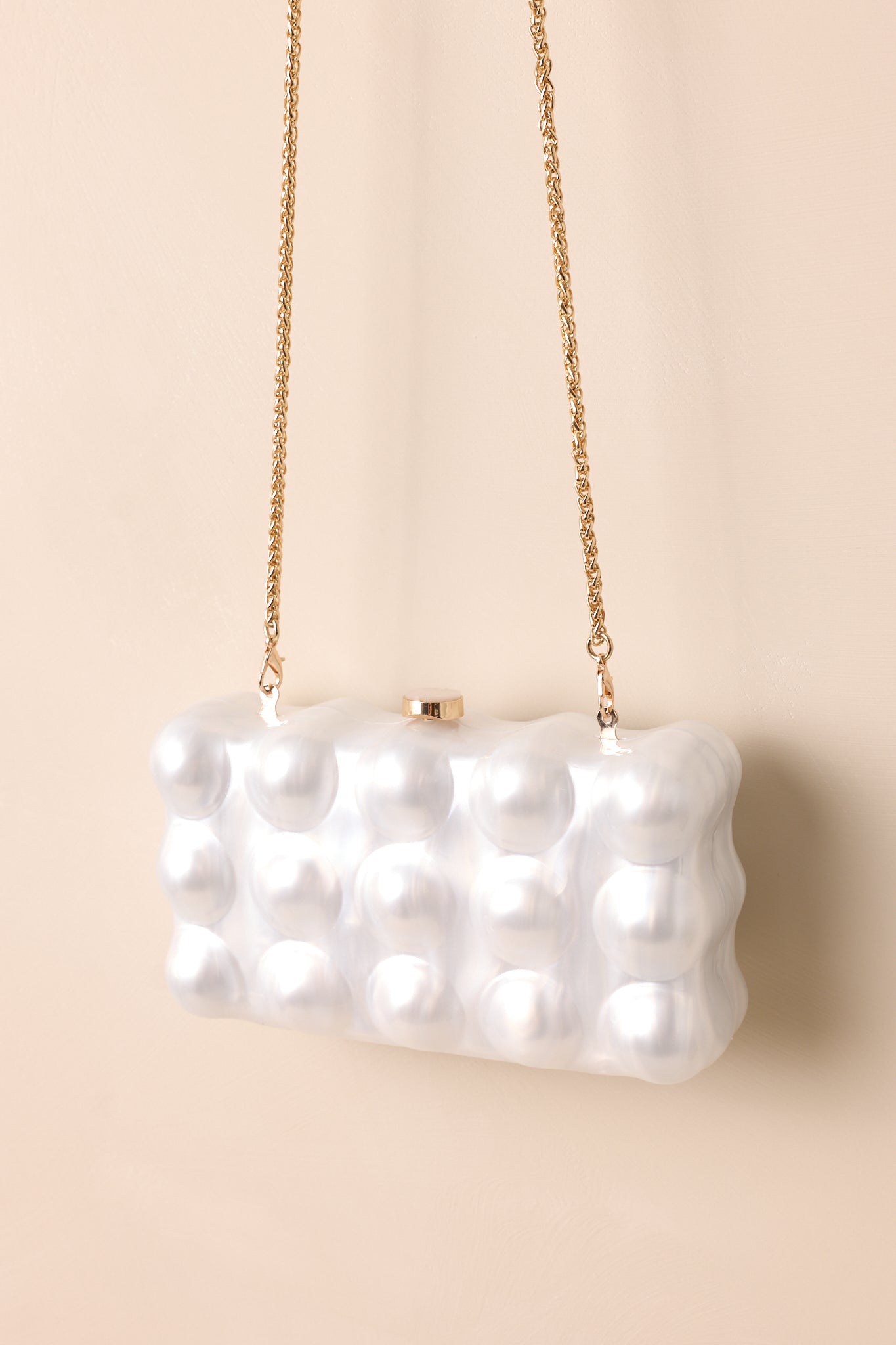 A stylish rectangular clutch featuring a pearl-like bubble texture and a gold chain strap, with a metallic clasp on top, hanging elegantly.