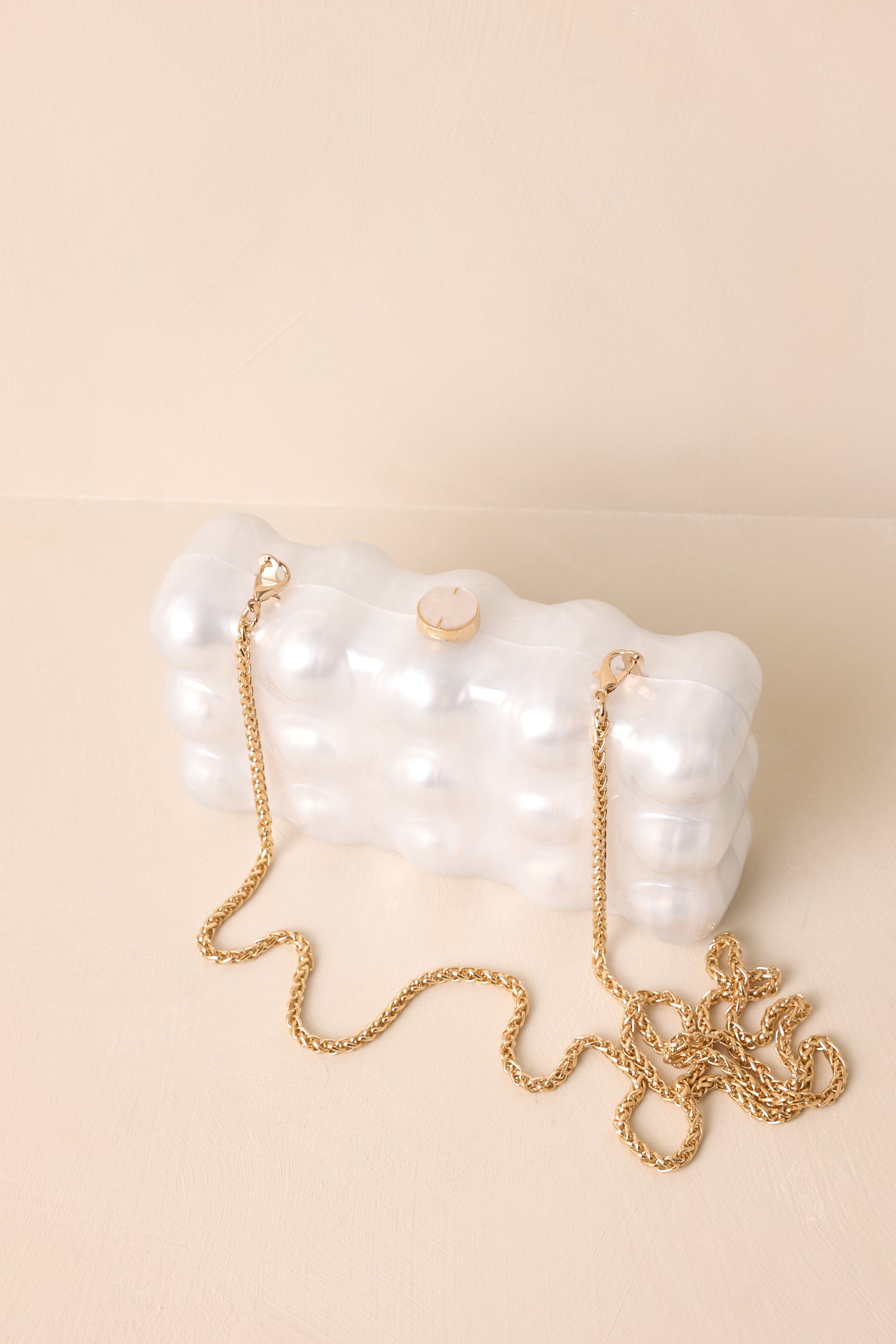 A close-up view of the clutch showcasing its glossy pearl-inspired bubble design and detachable gold chain, placed neatly on a neutral background.