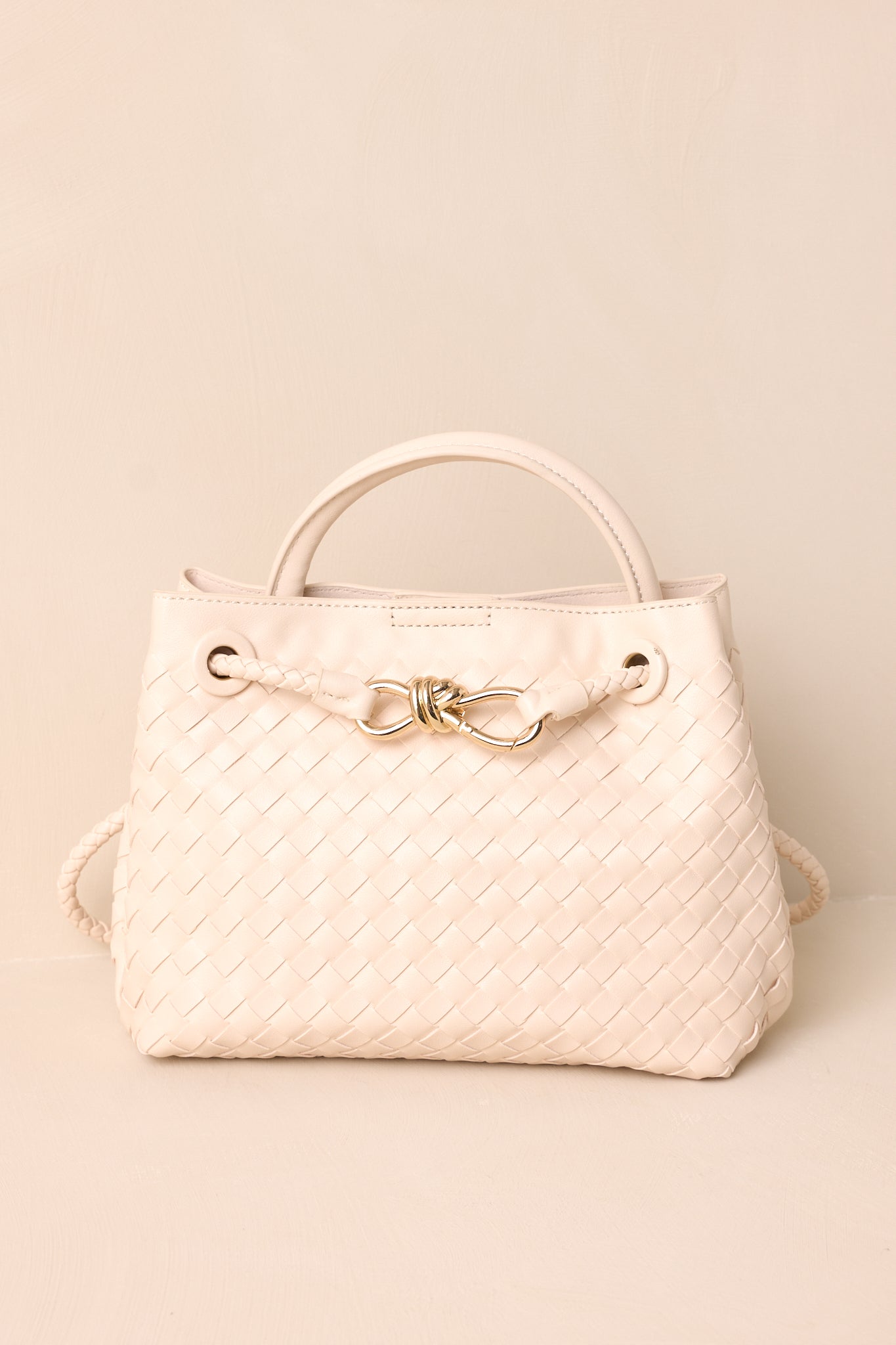 A side view of the ivory faux leather bag, highlighting the short handle for handheld use and the long removable woven strap for shoulder use.