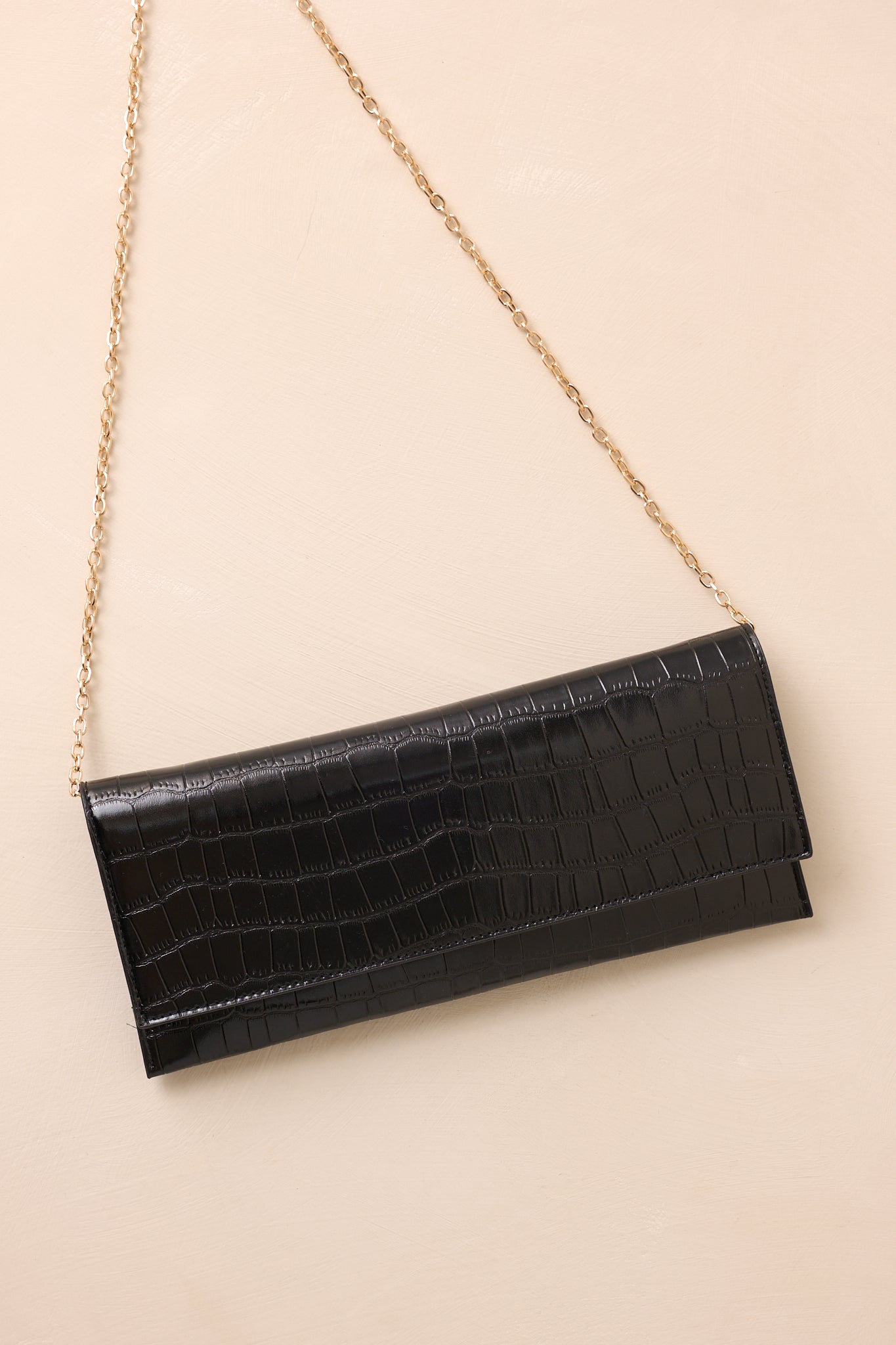 The black clutch laid flat with the optional gold chain strap displayed alongside the bag to emphasize its versatility.