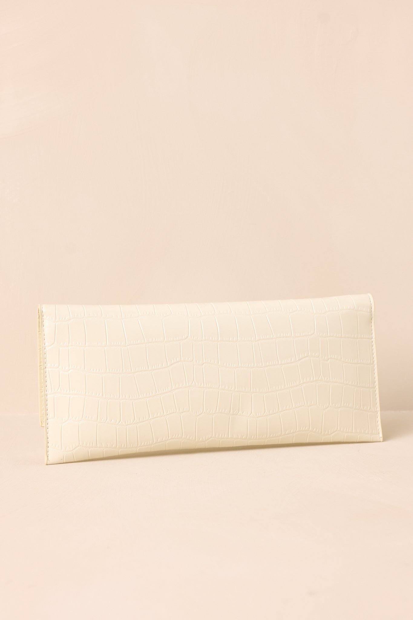 The back of the ivory clutch on a beige background, showing the continuous faux crocodile pattern with a smooth, clean design.