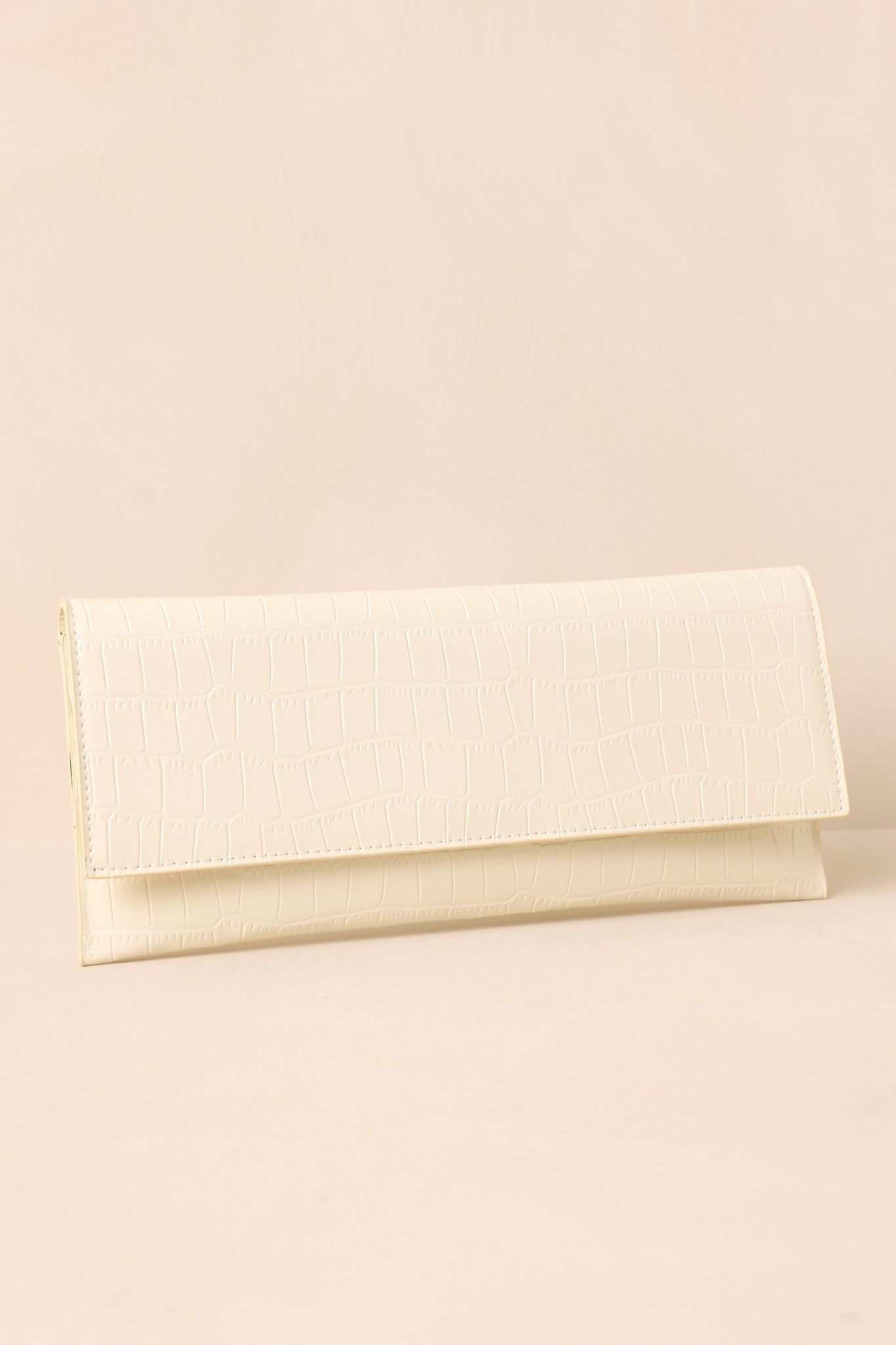 A side angle of the ivory clutch against a beige background, highlighting its slim profile.