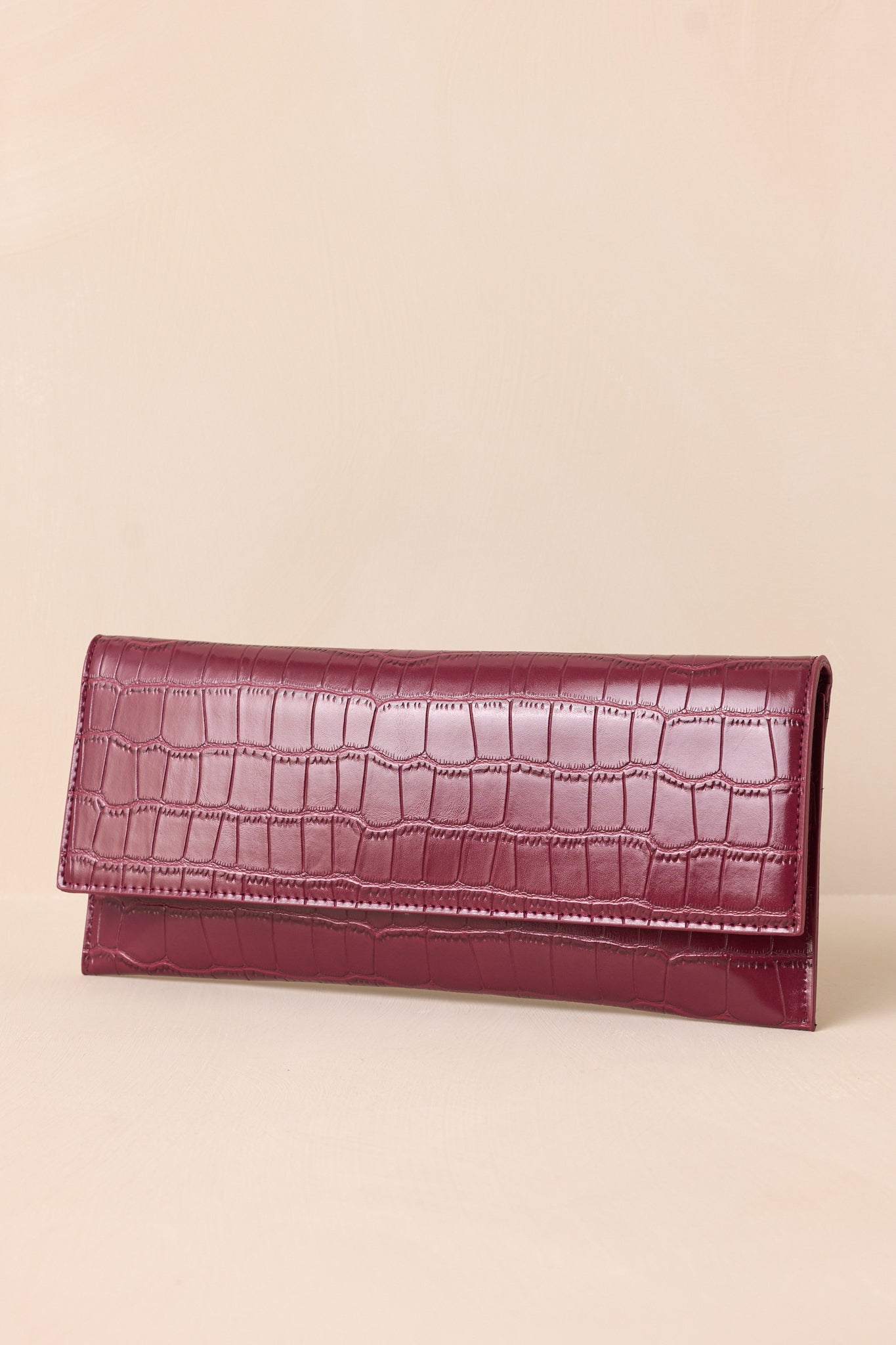 A side angle of the wine clutch against a beige background, highlighting its slim profile.