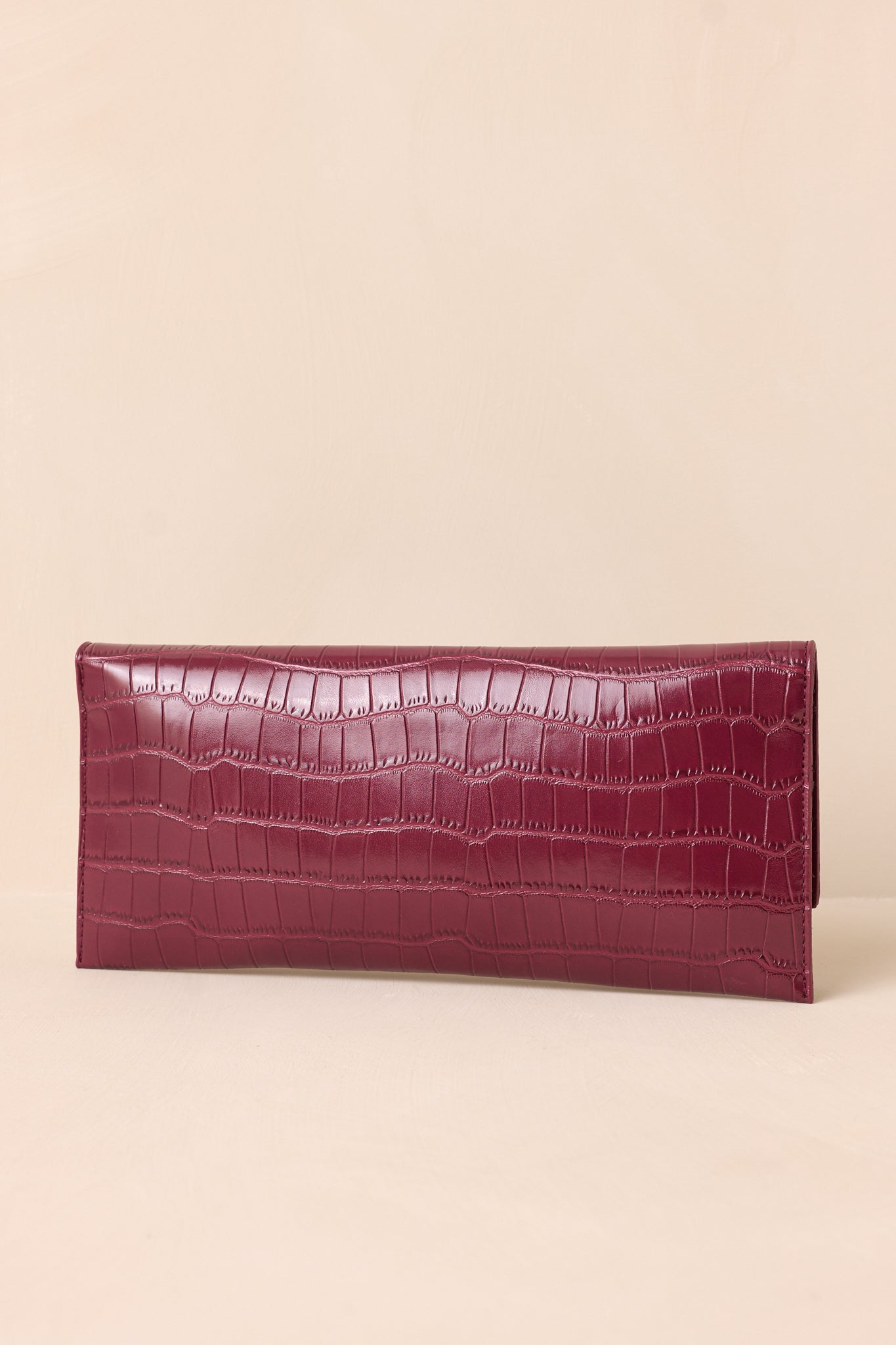 The back of the wine clutch on a beige background, showing the continuous faux crocodile pattern with a smooth, clean design.