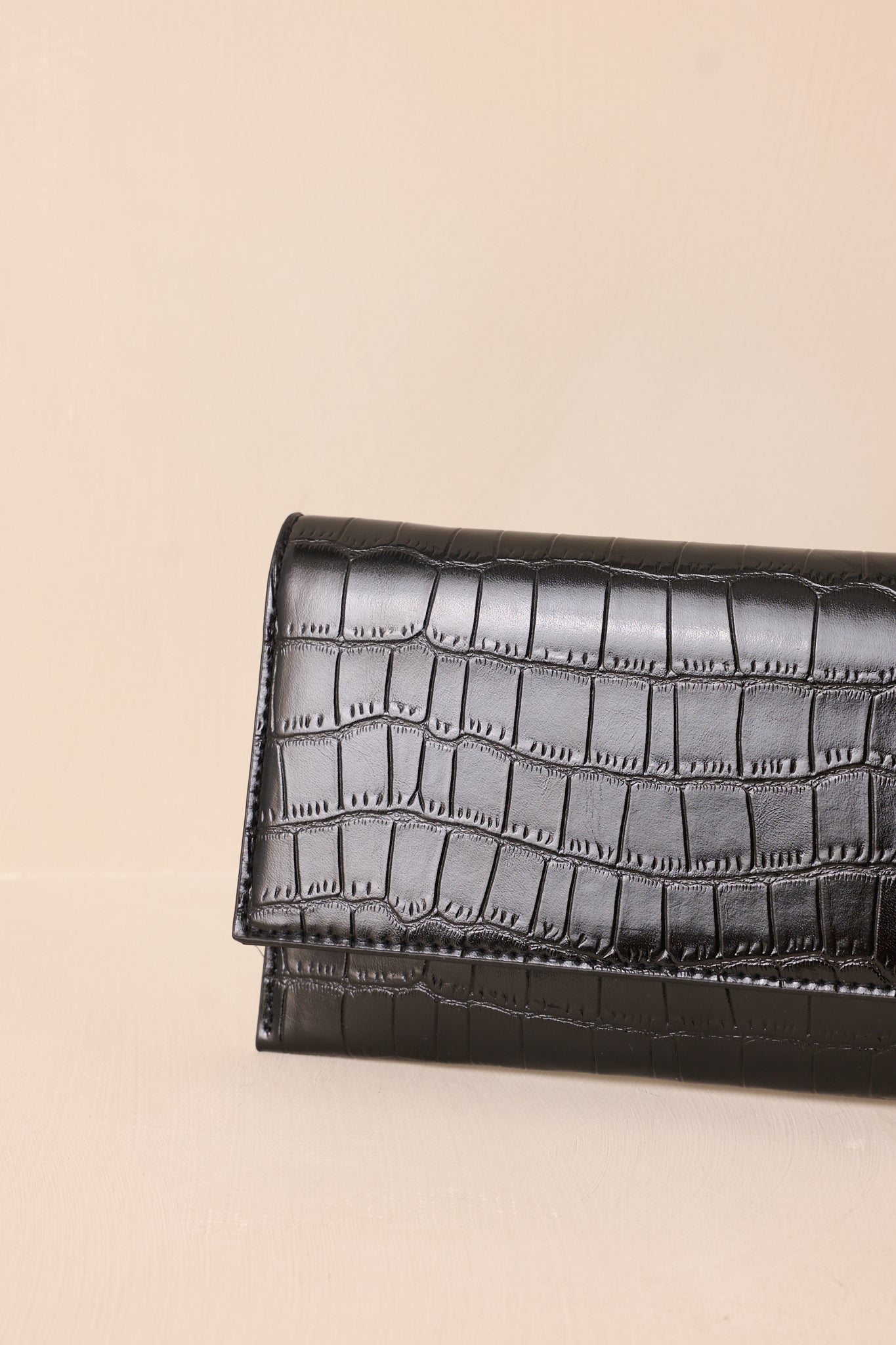 A close-up detail shot of the black clutch’s refined stitching of the faux crocodile material.