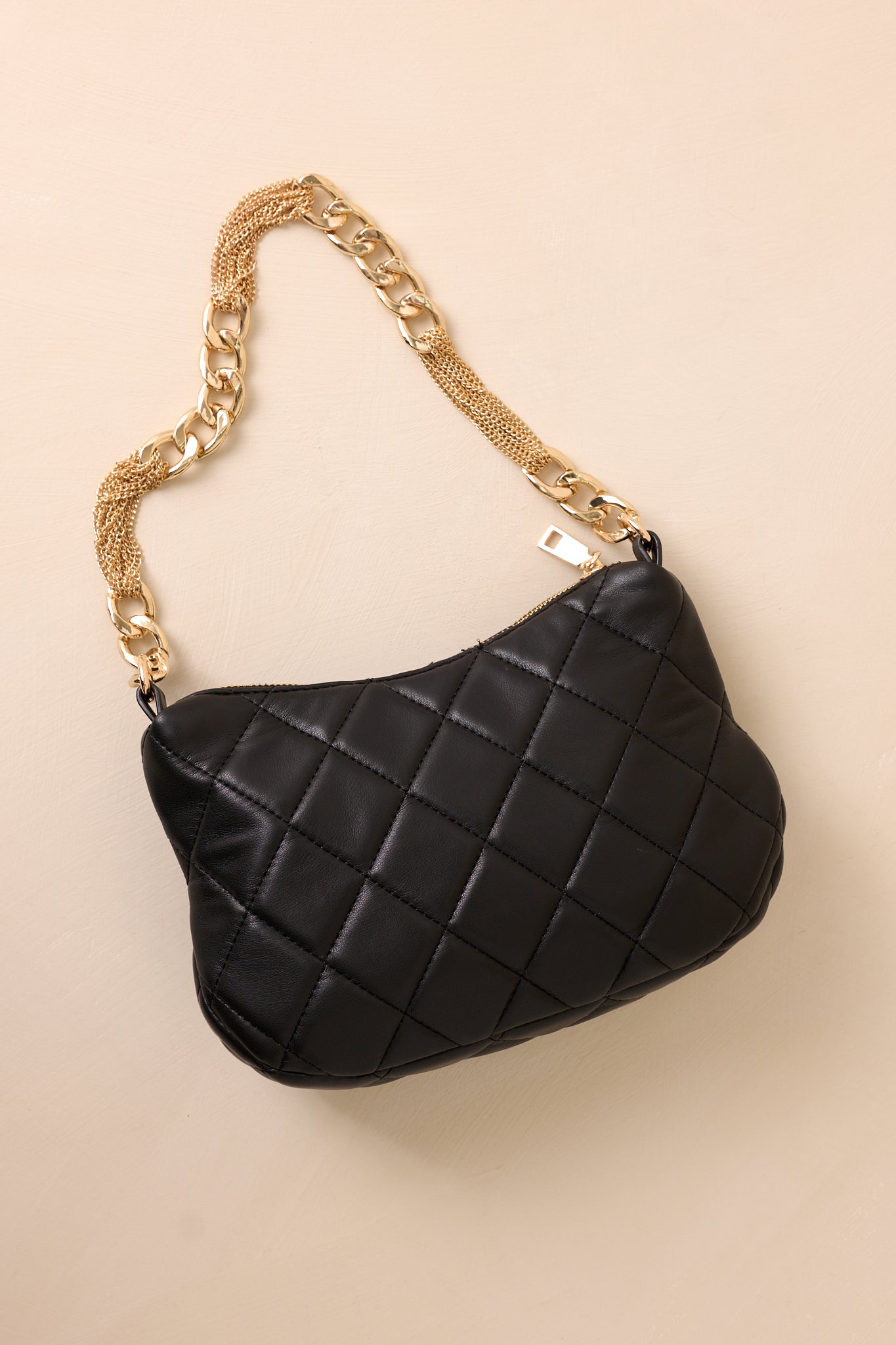 The black handbag laid flat against a beige background, revealing the smooth, unquilted back surface and the built-in zipper pocket for added functionality.