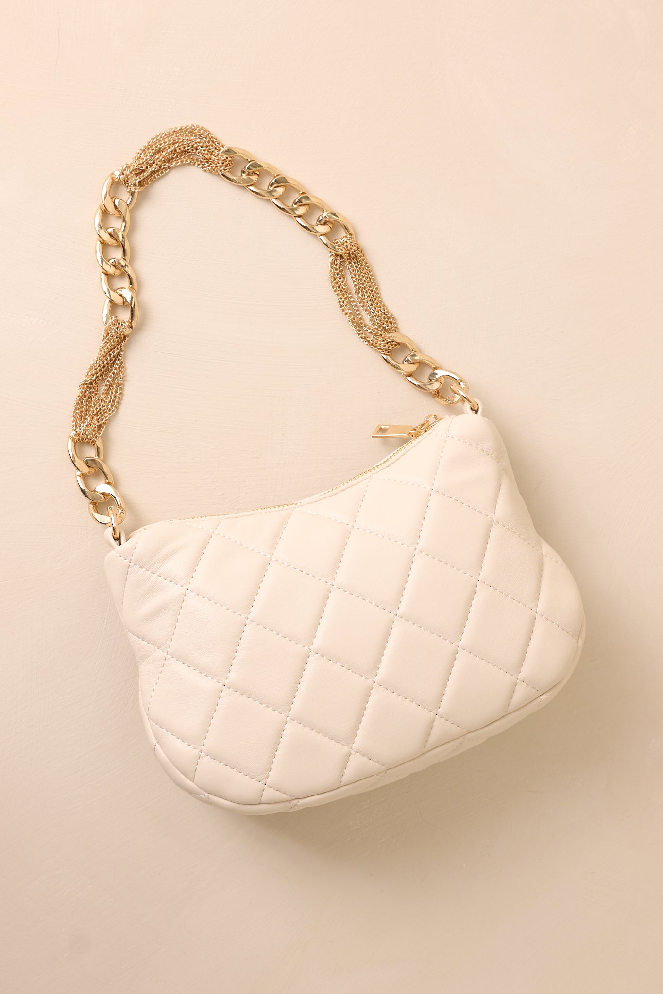 The ivory handbag laid flat against a beige background, revealing the smooth, unquilted back surface and the built-in zipper pocket for added functionality.