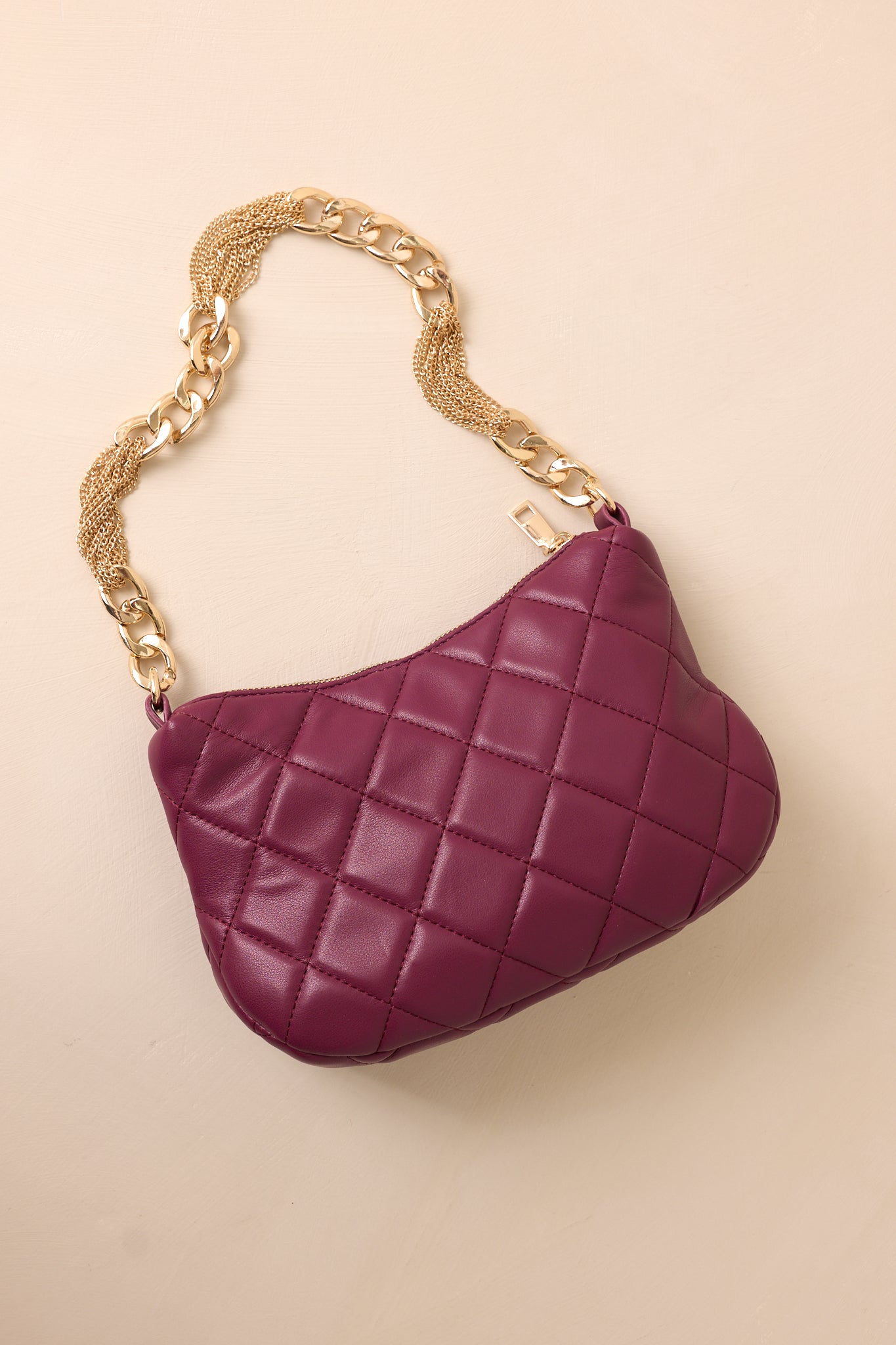 The merlot handbag laid flat against a beige background, revealing the smooth, unquilted back surface and the built-in zipper pocket for added functionality.