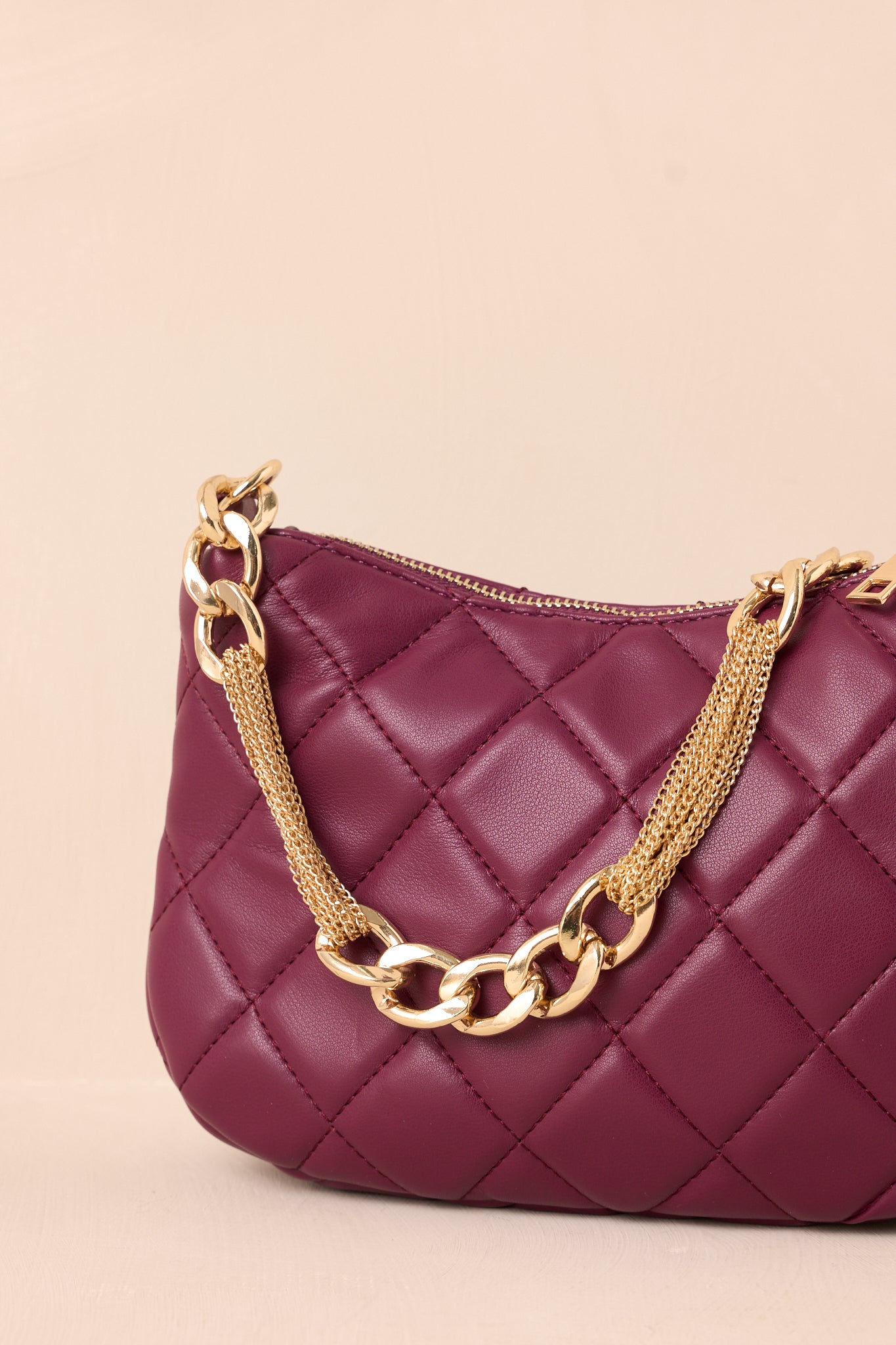 A detailed view of the merlot faux leather handbag, focusing on the fine quilted stitching, the gleaming gold zipper closure, and the attached thick gold chain handle.