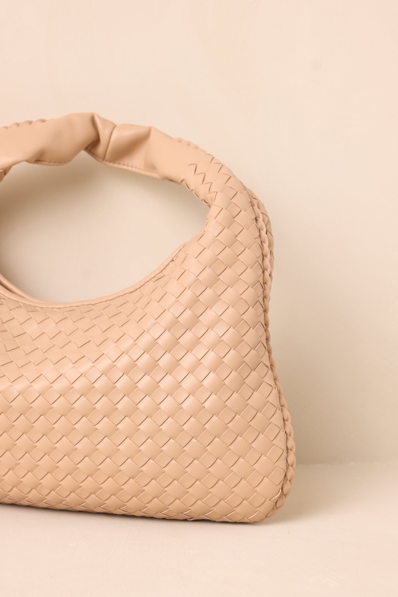 A close-up image focusing on the gold zipper closure of the tan handbag, with the woven texture and faux leather handle in the background.