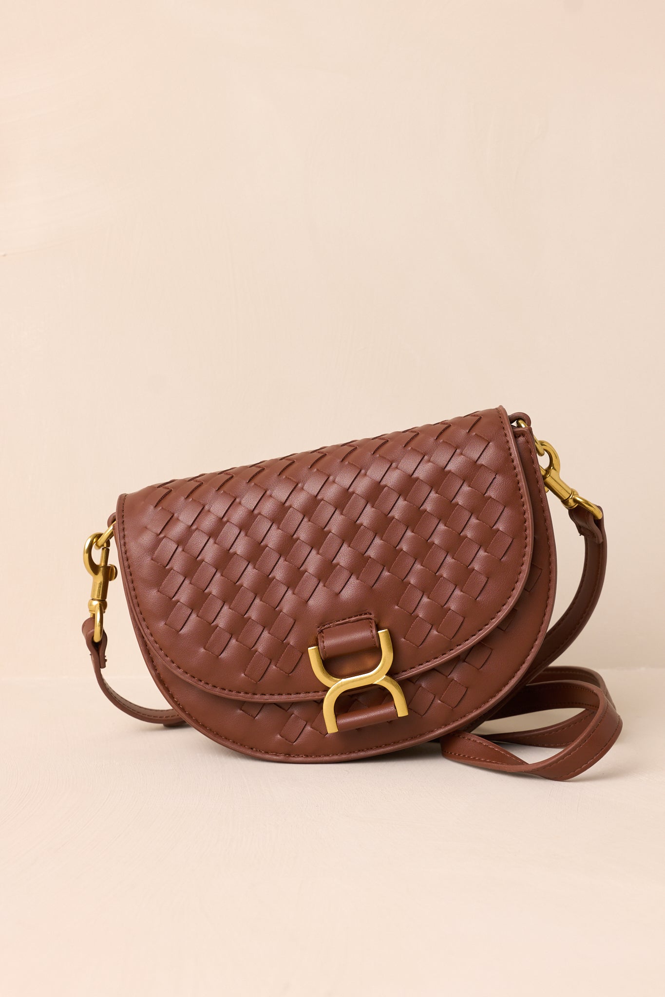 A side angle of the brown handbag on a beige background, highlighting the solid brown belt-style shoulder strap and the structured silhouette of the design.