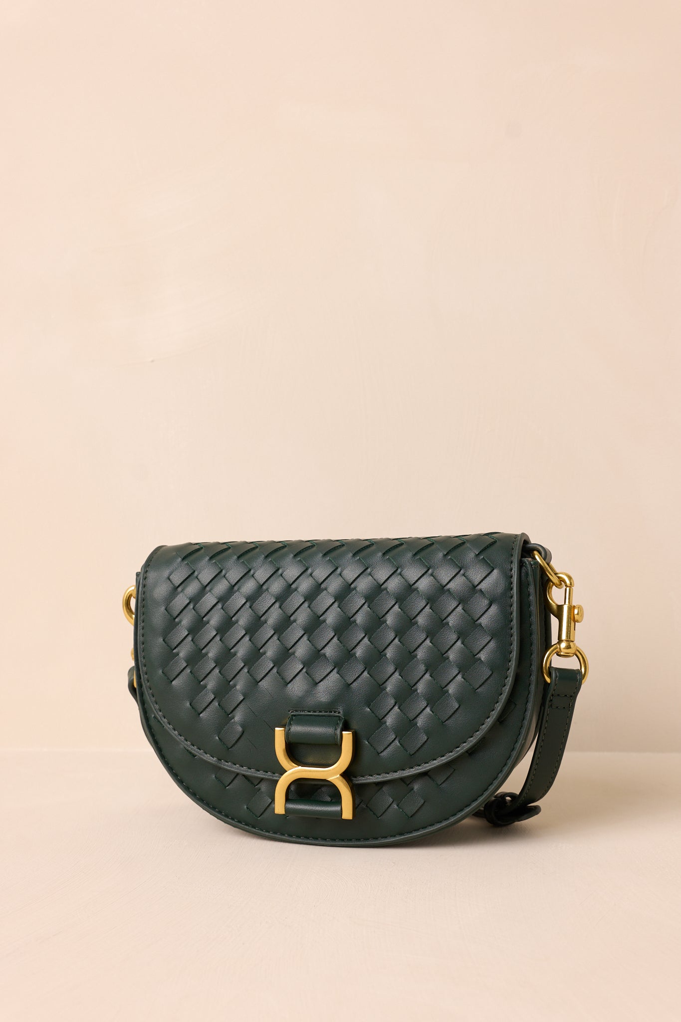 The green handbag displayed upright against a beige background, showcasing its fold-over design, gold buckle snap closure, and woven faux leather material.