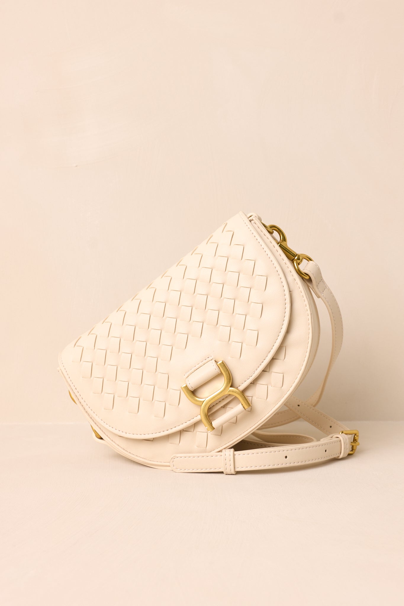 A side angle of the beige handbag on a beige background, highlighting the solid beige belt-style shoulder strap and the structured silhouette of the design.