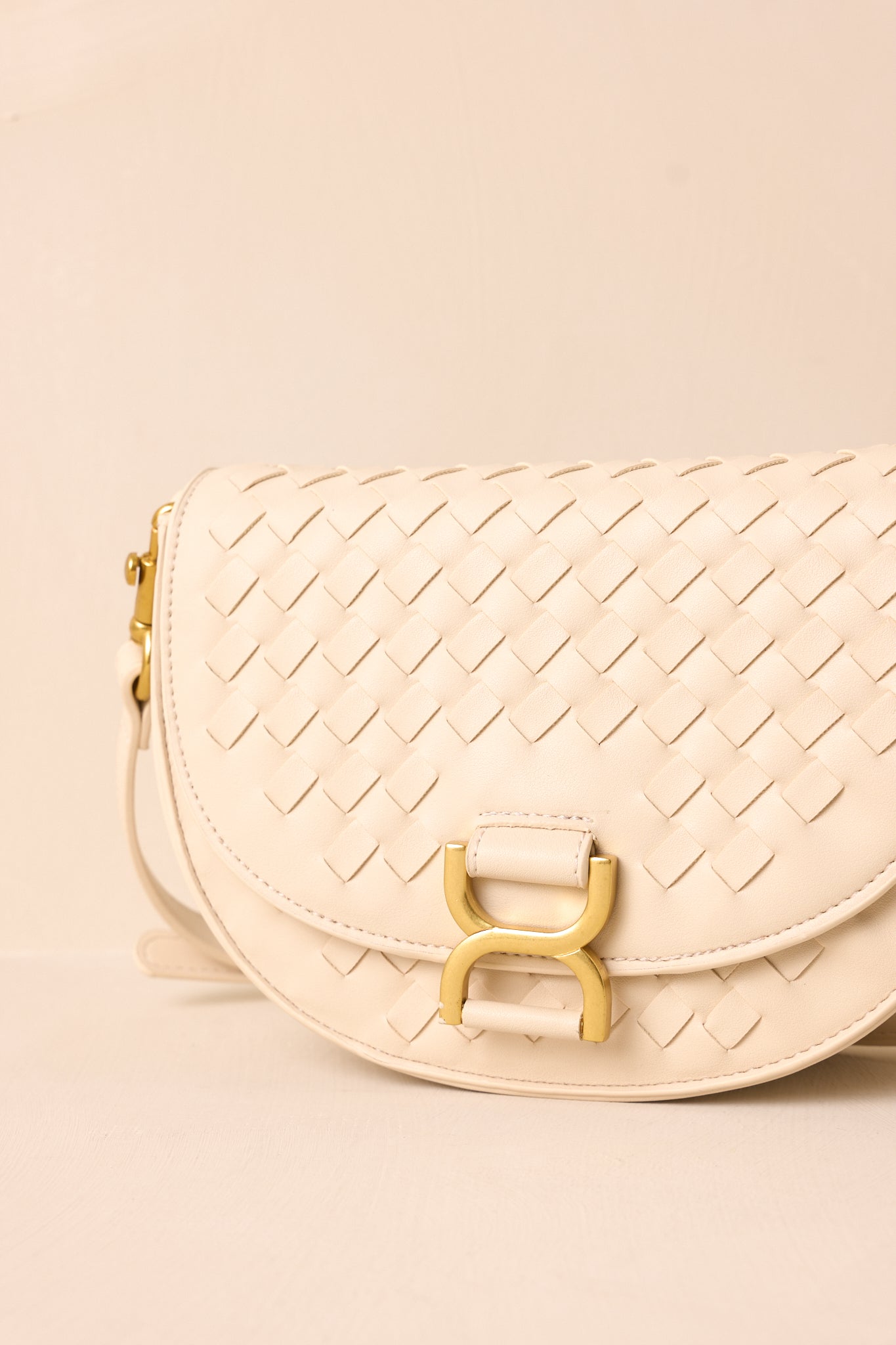 An extreme close-up of the handbag, showcasing the gold hardware, the woven faux leather texture, and the edge of the built-in inside pouch peeking out.