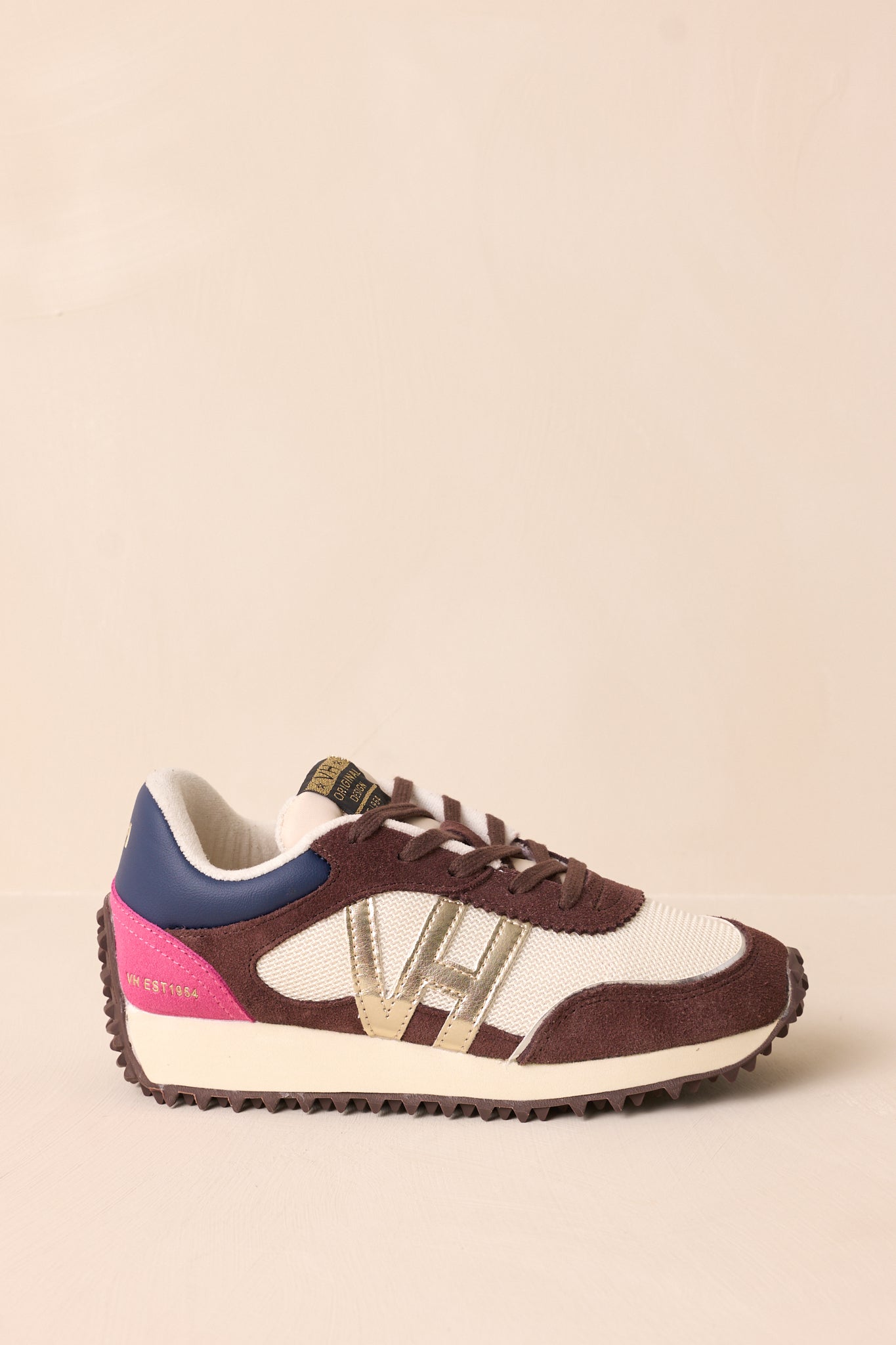 A side angle of the chocolate multi sneakers on a beige background, showcasing the pops of pink and blue accents, gold detailing on the side, and the slightly elevated platform sole.