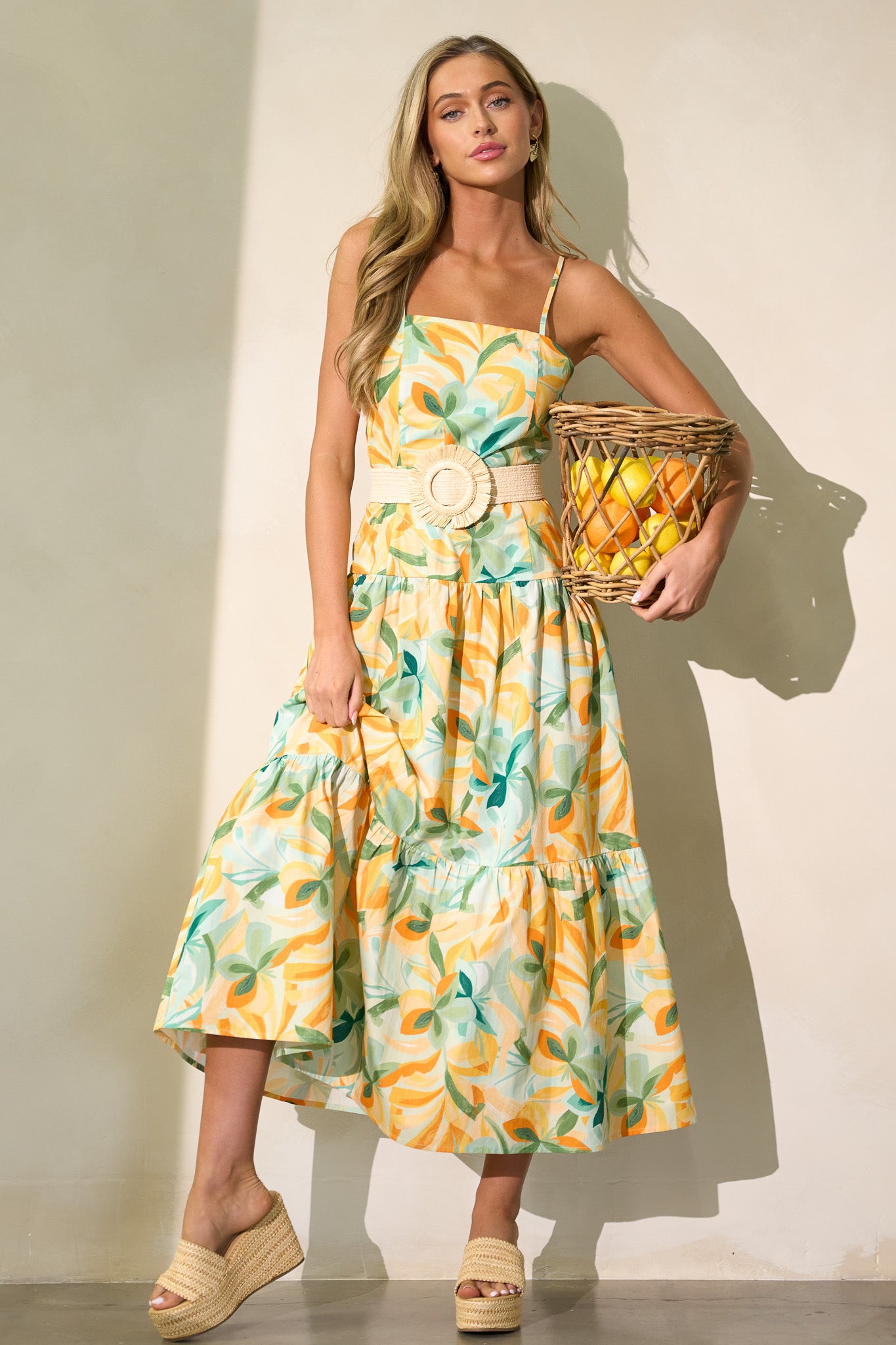 This yellow midi dress features a square neckline, a discreet side zipper, a smocked back insert, a tiered design, and a flowing silhouette.