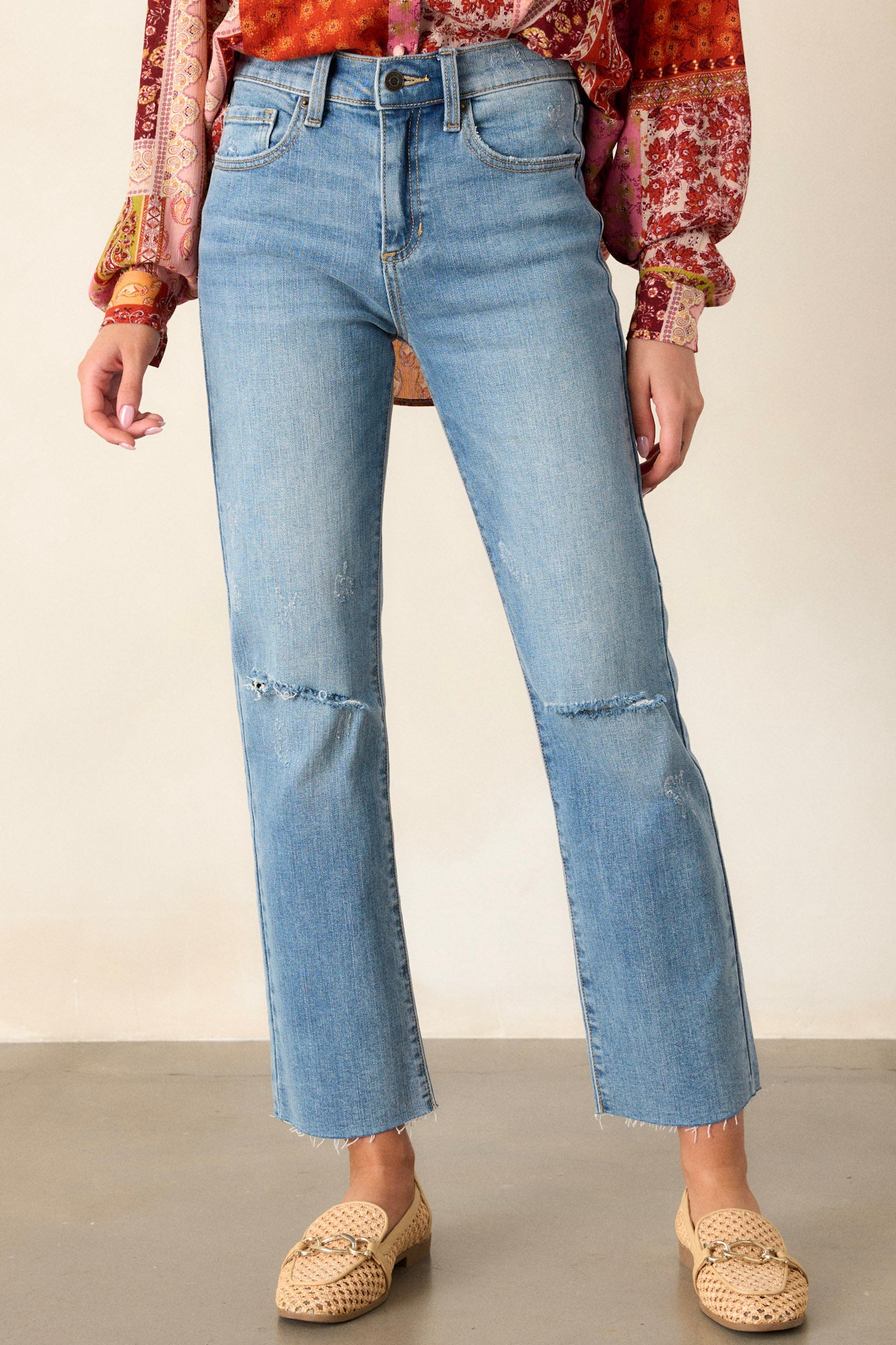 Front view of jeans featuring a high waisted design, button and zipper closure, belt loops, functional front and back pockets, distressing, and a raw hemline.