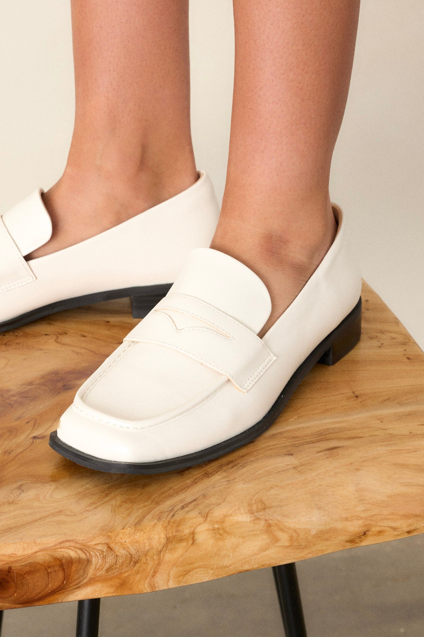 These white loafers feature a slip on design, a small heel, a square toe, and a strap across the foot.