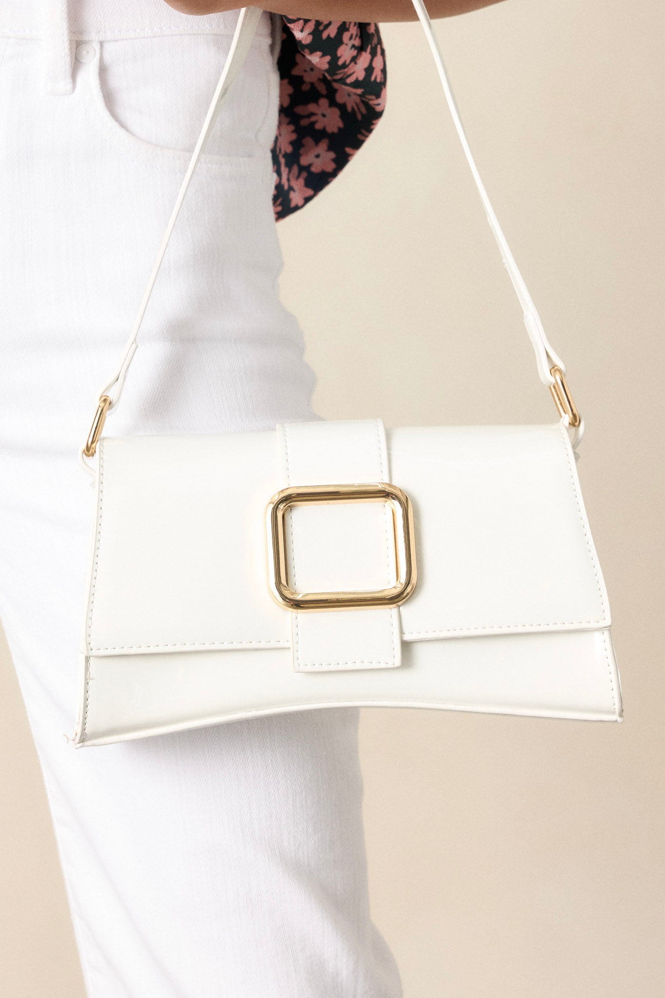 This white handbag features a gold rectangular buckle, two snap clasps, interchangeable straps and a glossy chic design.