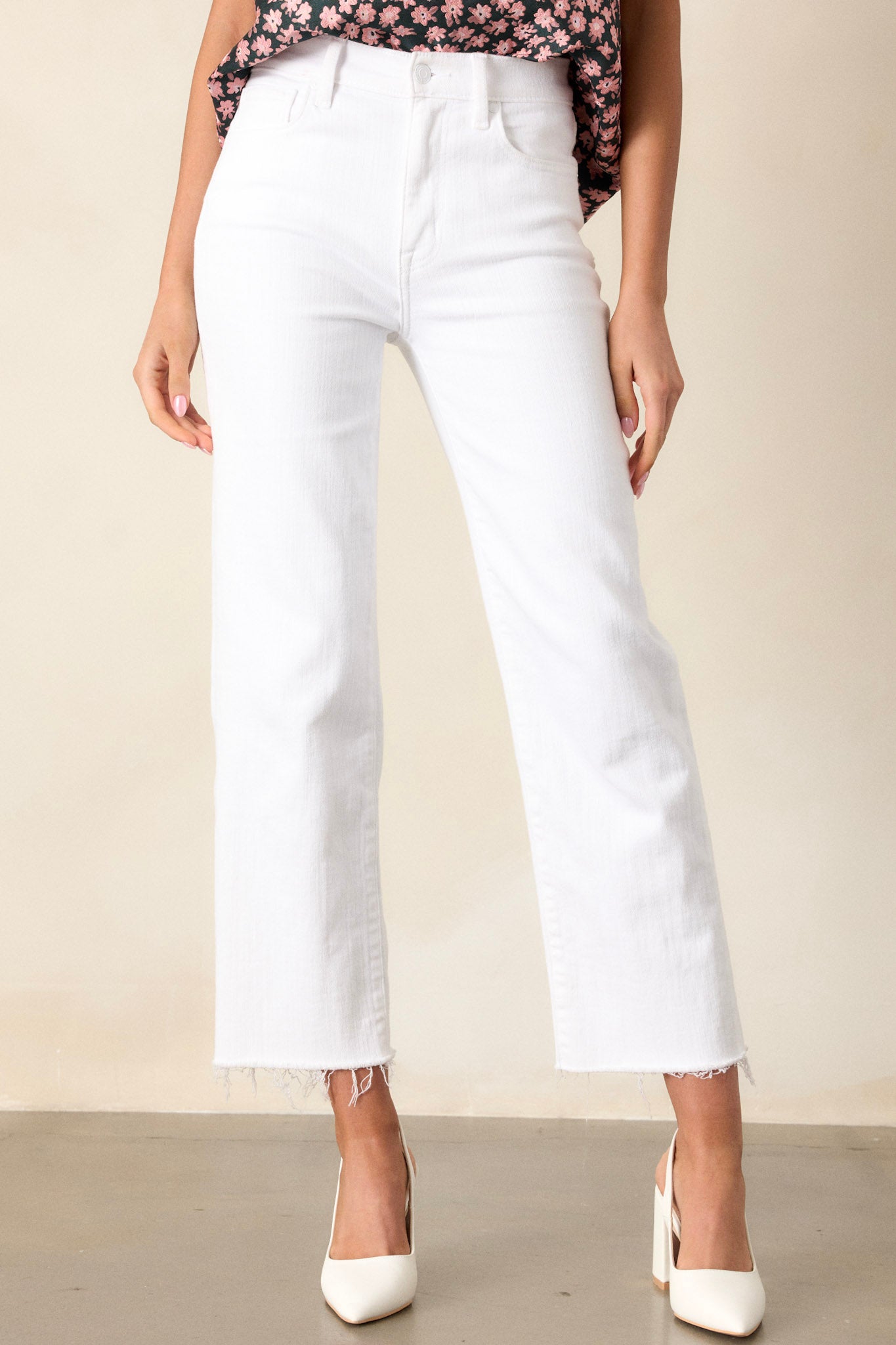 Front view of white jeans featuring a high waisted design, classic button and zipper closure, belt loops, functional front and back pockets, a cropped length, and a raw hemline.