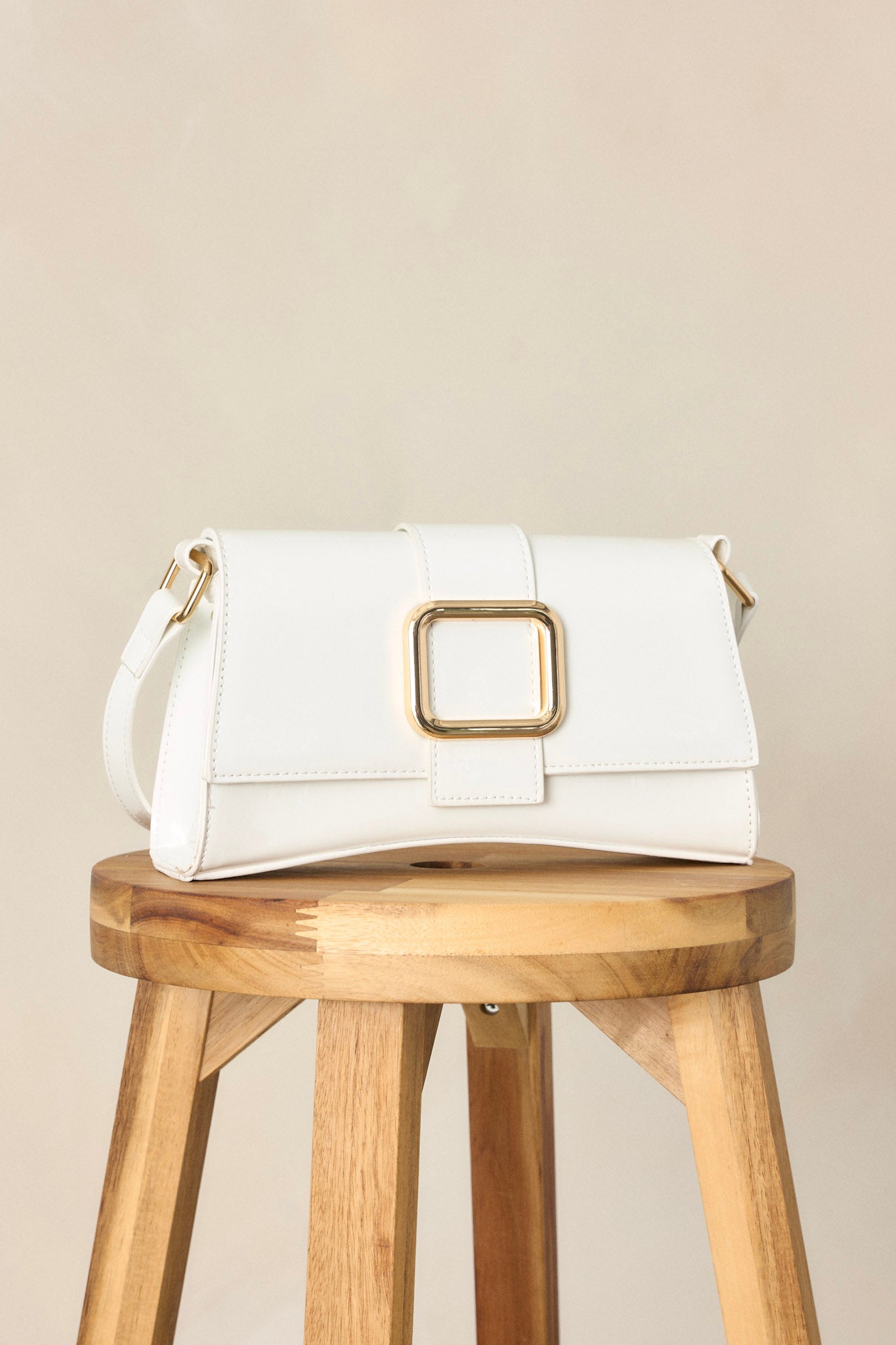 Close-up view of this white handbag featuring a gold rectangular buckle, two snap clasps, interchangeable straps and a glossy chic design.