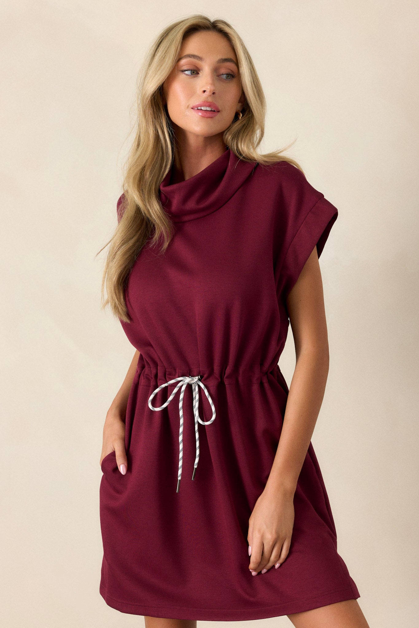 Short sleeve burgundy dress with a drawstring waist, cowl turtleneck, and functional pockets for a chic, casual vibe.