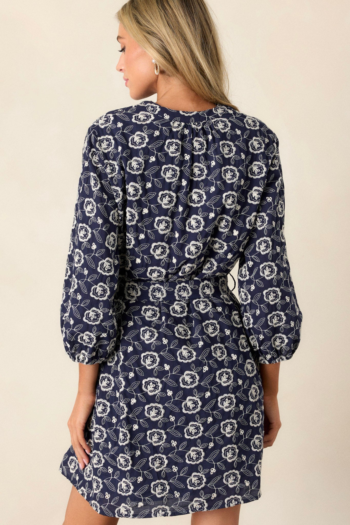 The back of the navy mini dress features the embroidered floral print and elastic cuff long sleeves, with a slight gathering at the waist due to the self-tie belt..