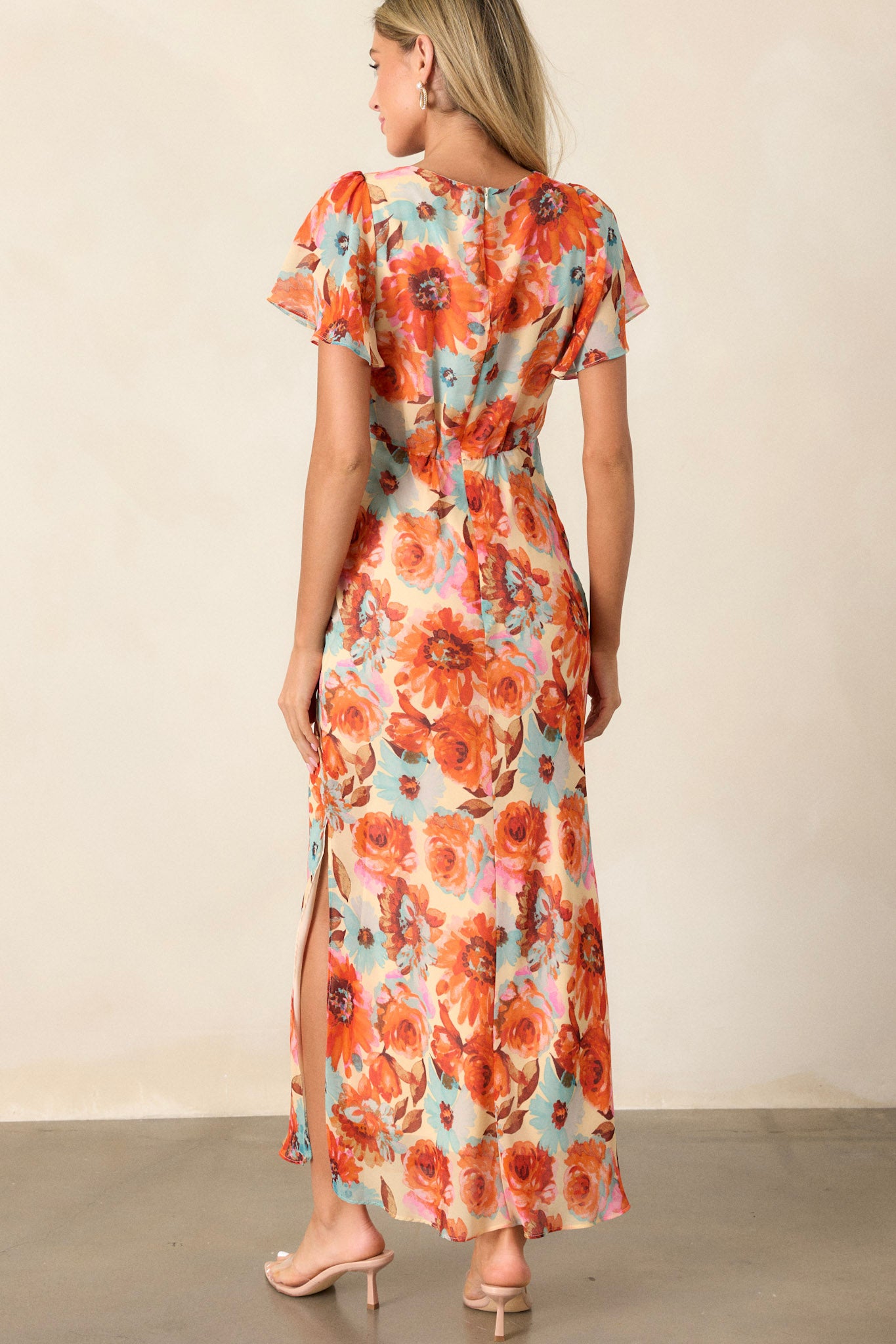 Back view of an orange floral dress highlighting the discrete back zipper, elastic waist insert, and the sheer short sleeves.