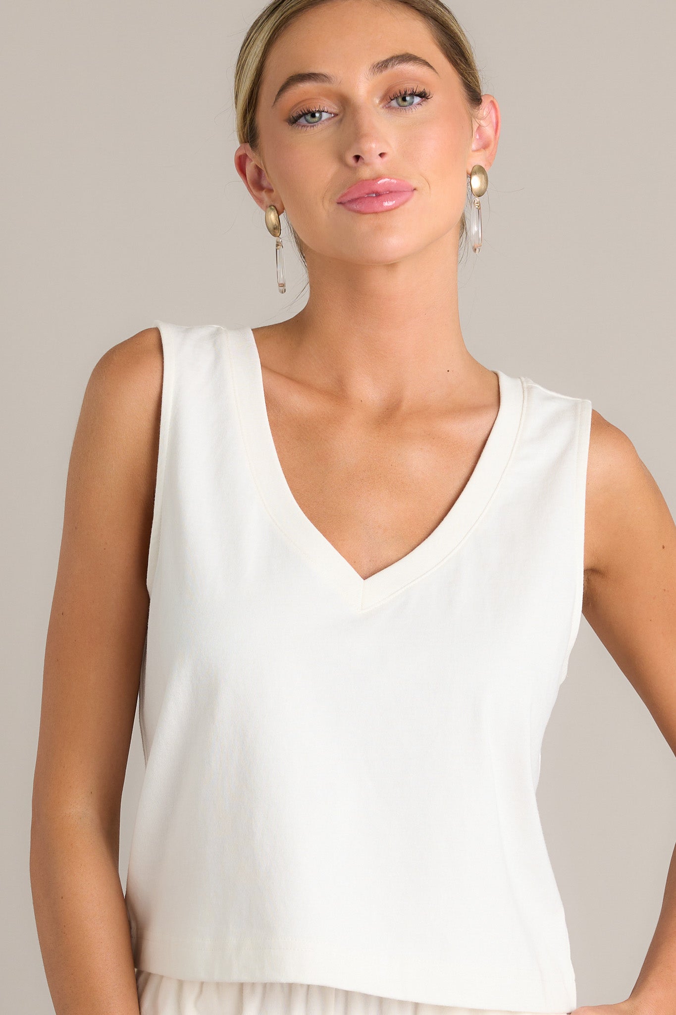 This white tank features a v-neckline, a sleeveless design, and a slightly cropped hemline.