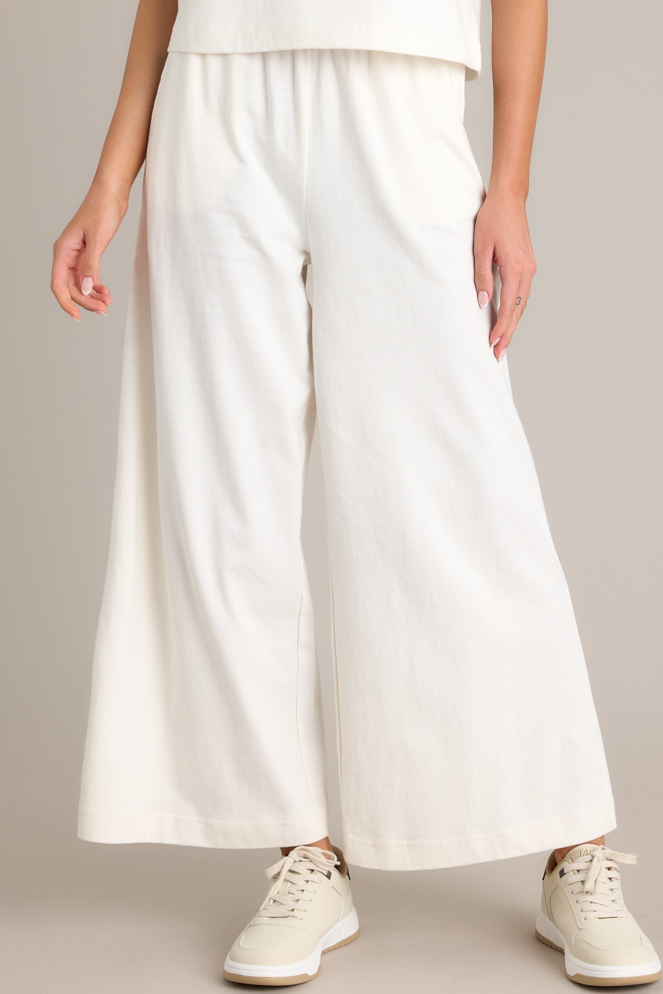 Front view of these white flare pants featuring an elastic waistband, functional pockets, a wide leg design, and a soft jersey material.