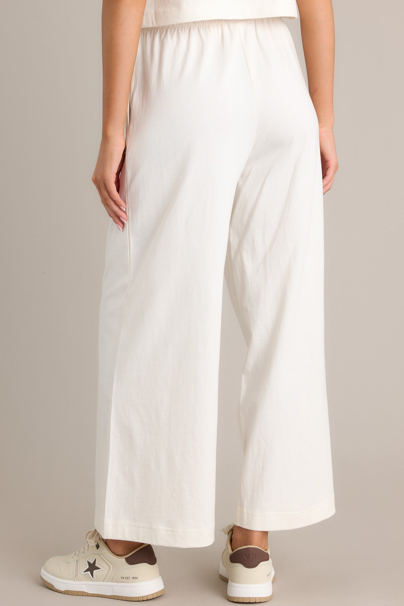 Back view of these white flare pants featuring an elastic waistband, functional pockets, a wide leg design, and a soft jersey material.