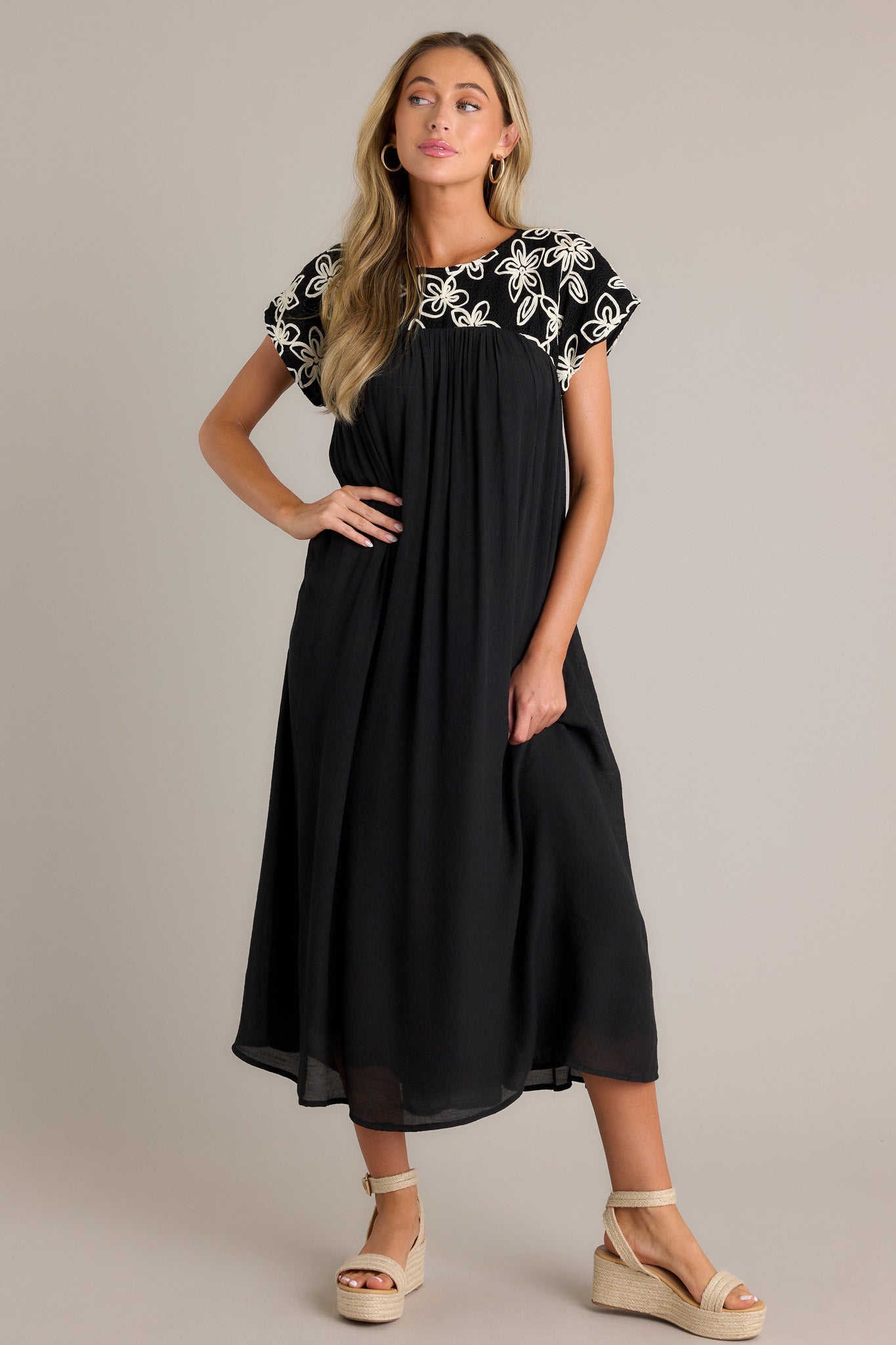 Black midi dress with a high rounded neckline, detailed with an embroidered floral pattern and a flowing silhouette.