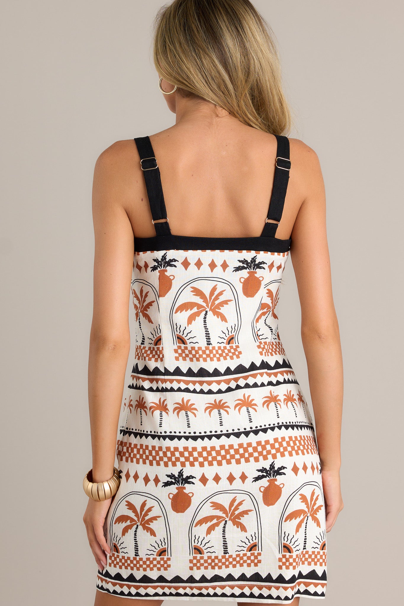 Back view of a beige mini dress highlighting the adjustable straps, playful palm print, and overall fit.