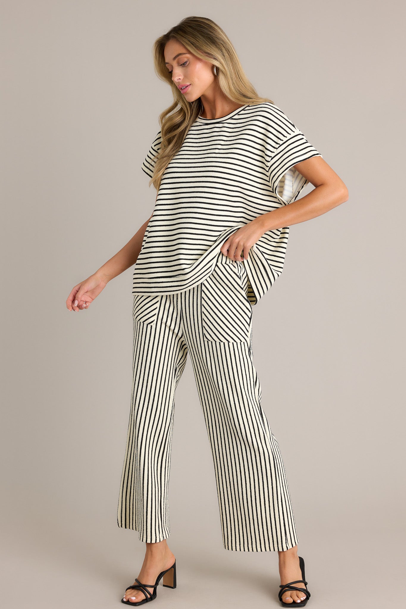 Side view of black stripe pants showcasing the high waisted design, elastic waistband, self-tie drawstring, functional hip pockets, and wide leg.