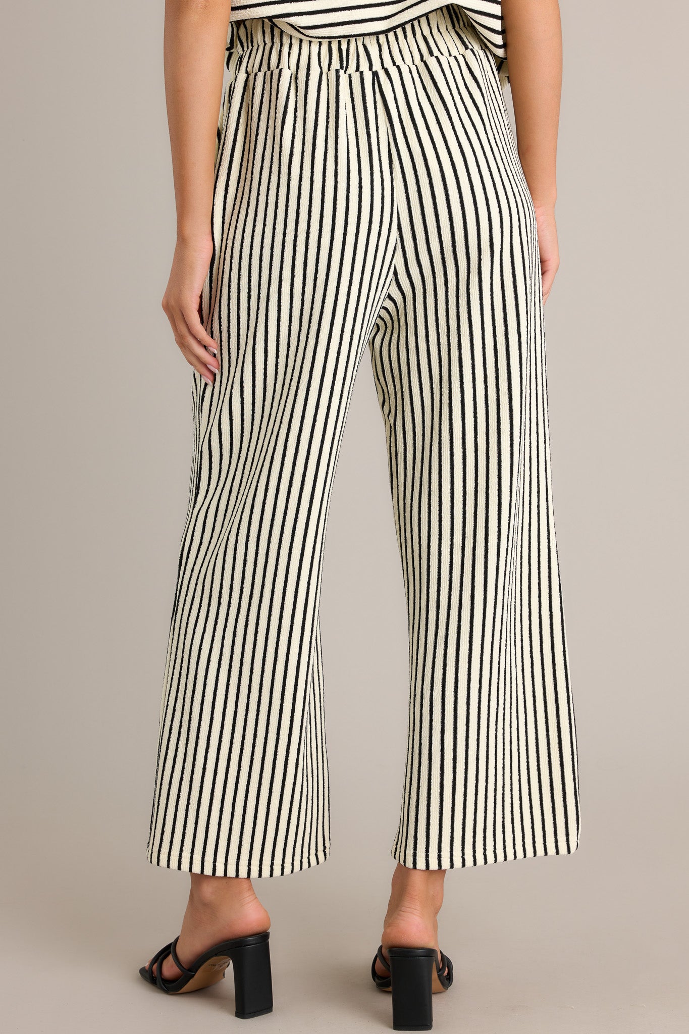 Back view of black stripe pants highlighting the overall fit, elastic waistband, and wide leg.