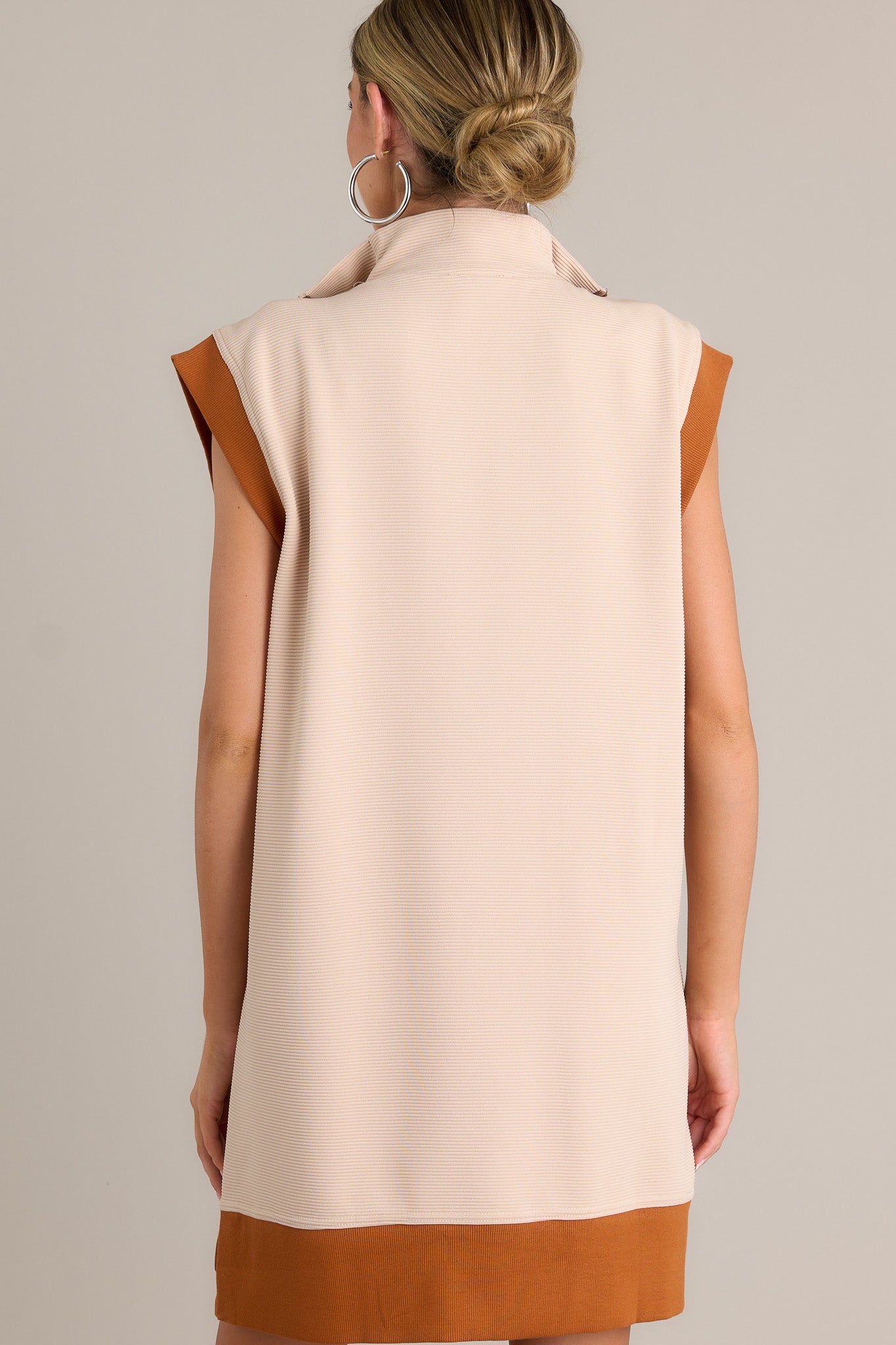 Back view of this taupe mini dress featuring a collared v-neckline, a functional zipper front, ribbed detailing, functional front pockets, a split hemline, a short cap sleeves.