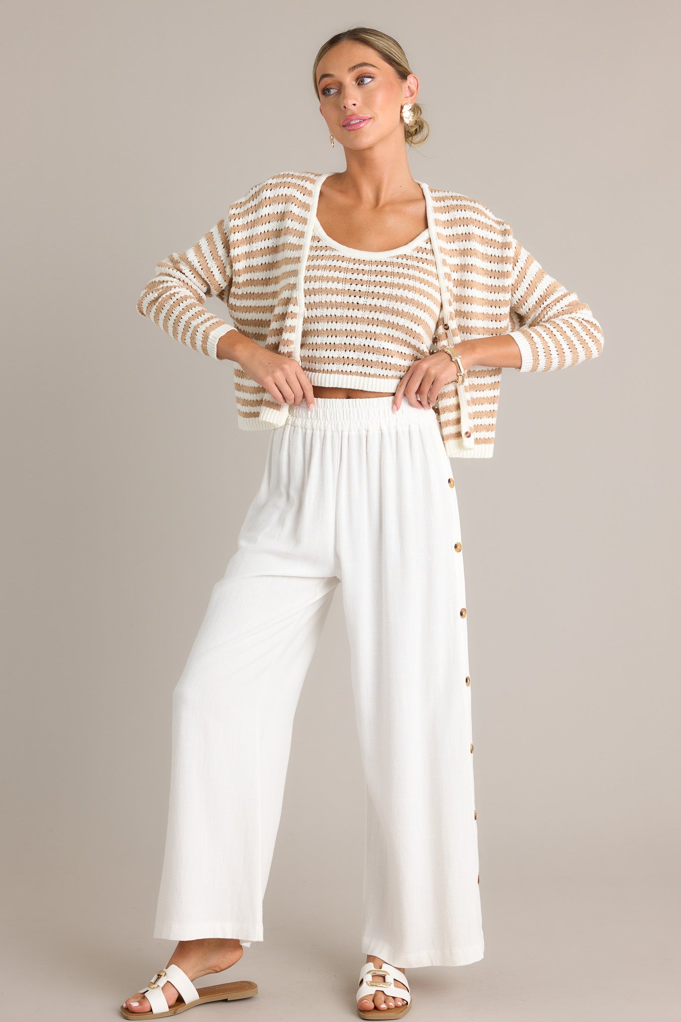 Front view of these ivory pants featuring a high waisted design, an elastic waistband, functional buttons all down the sides, a lightweight material, and a wide leg.