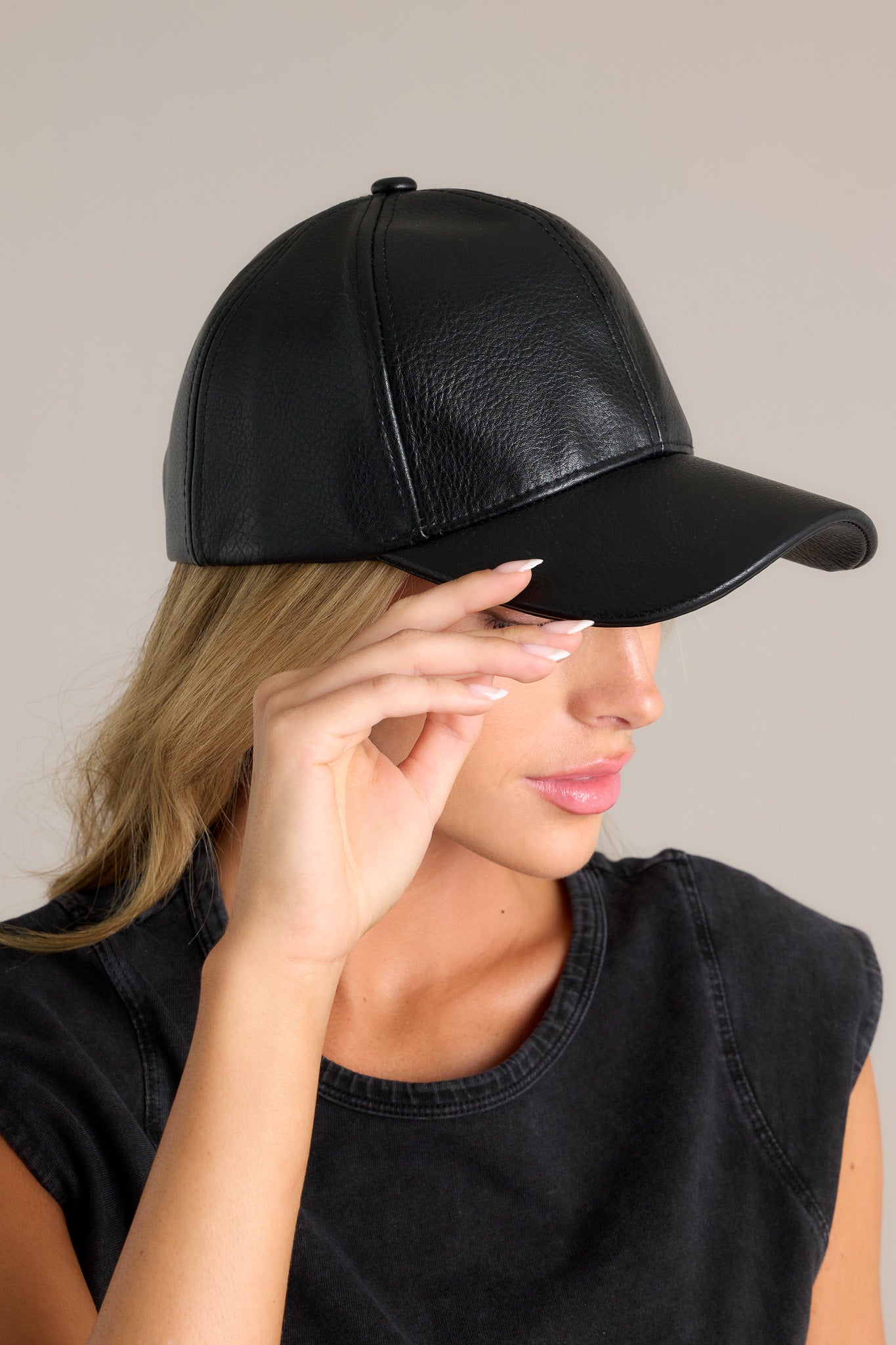 Side view of this all black hat featuring a faux leather material, and an adjustable velcro strap in the back.